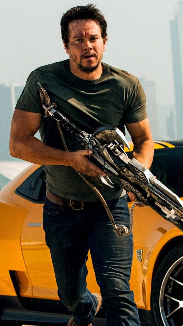 Mark Wahlberg 桌布 壁紙 — 馬克·華伯格帶著未來武器，在一輛亮黃色跑車旁邊緊急奔跑，背景是模糊的城市天際線。