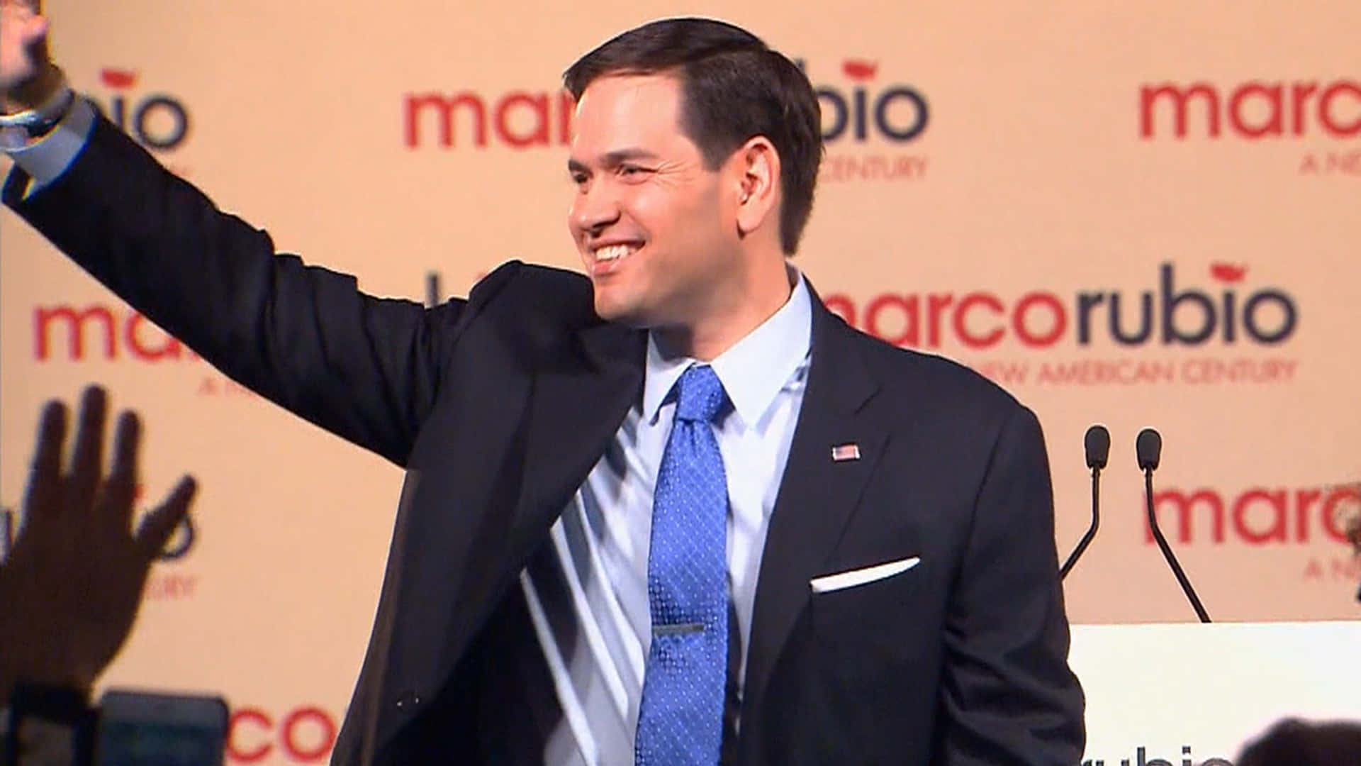 Celebrity 桌布 壁紙 — 馬可·魯比奧在帶有「marcorubio」品牌背景的競選活動中熱情地向支持者揮手。