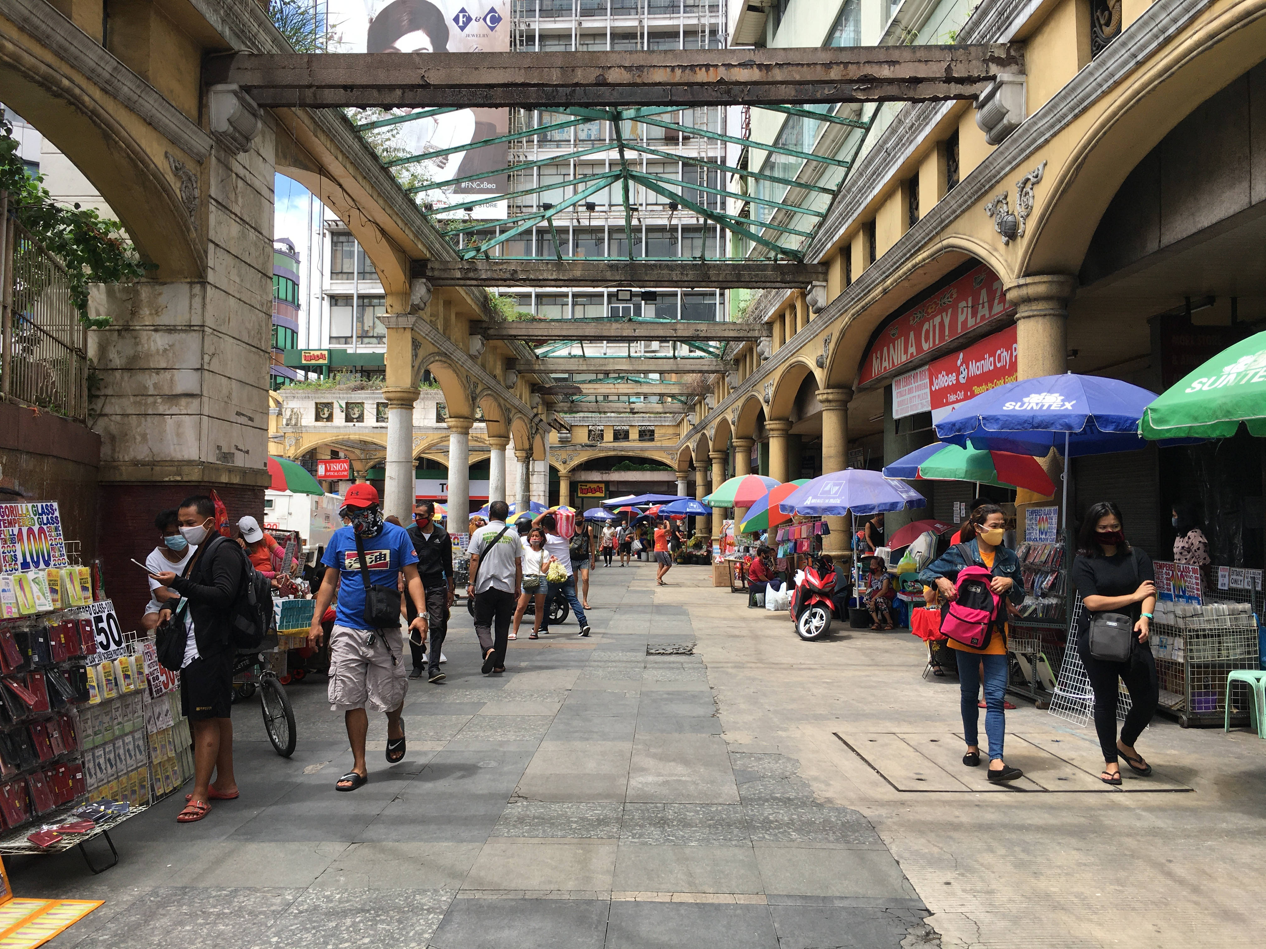 Philippines 桌布 壁紙 — 馬尼拉城市廣場一條熱鬧的有蓋行人街，購物者經過拱形柱廊下色彩繽紛的攤位。