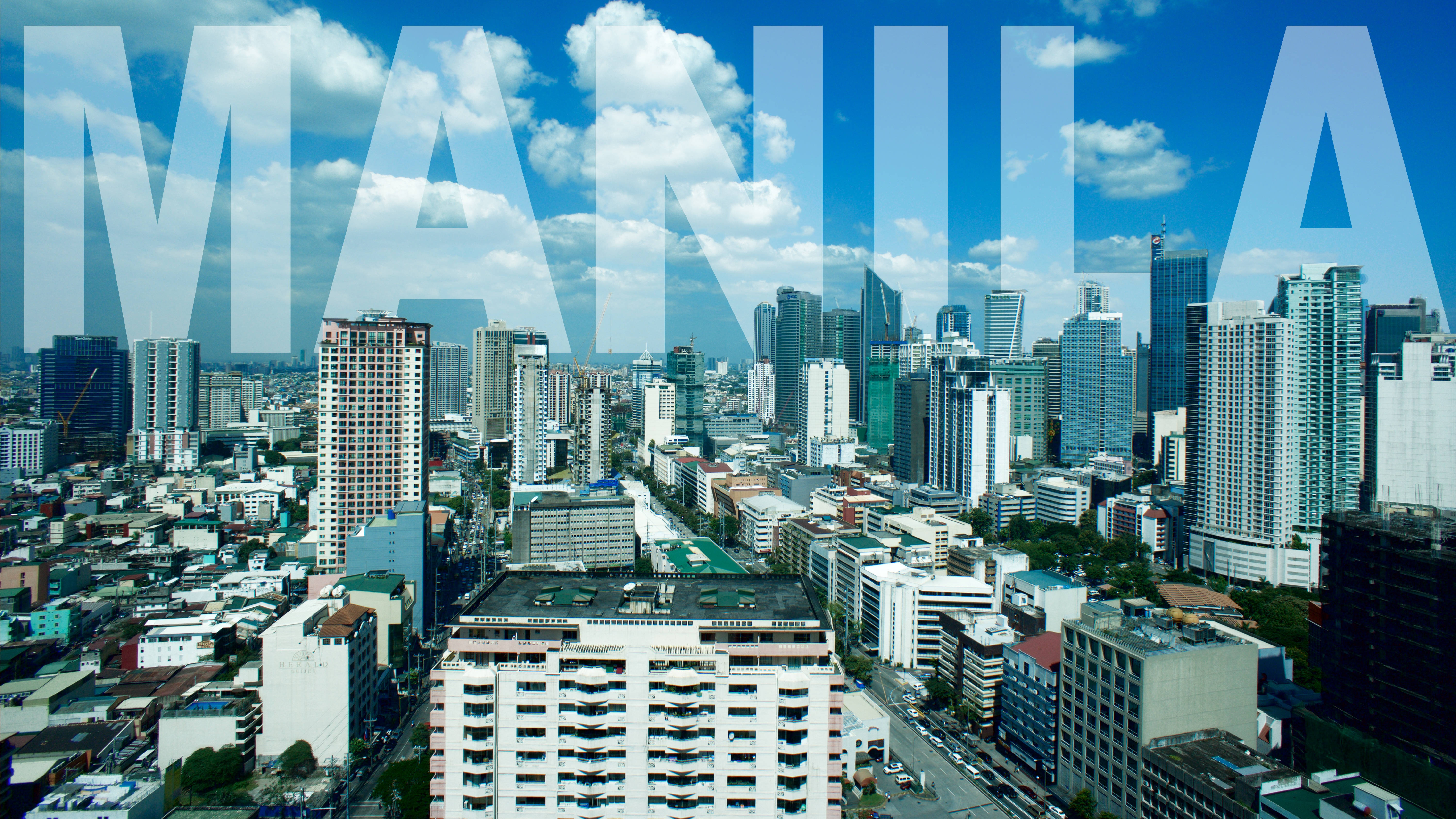 Manila 桌布 壁紙 — 馬尼拉城市景觀的鳥瞰圖，高聳的摩天大樓和密集的城市建築，在明亮的藍天和蓬鬆的白雲下。