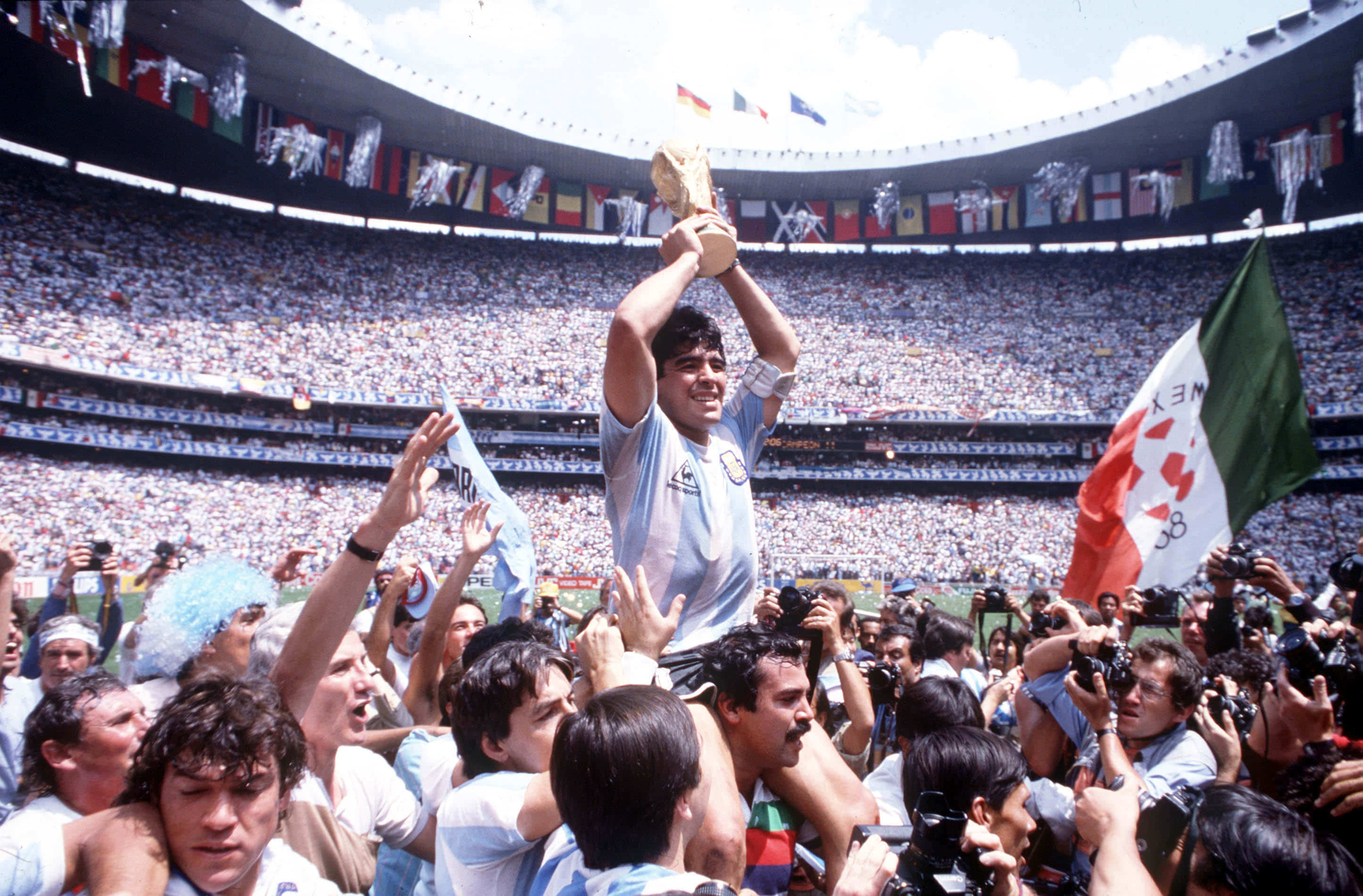 FIFA 世界盃 桌布 壁紙 — 馬拉度納高舉世界盃獎盃在頭頂，喜悅的隊友和球迷在擠滿的球場上慶祝。