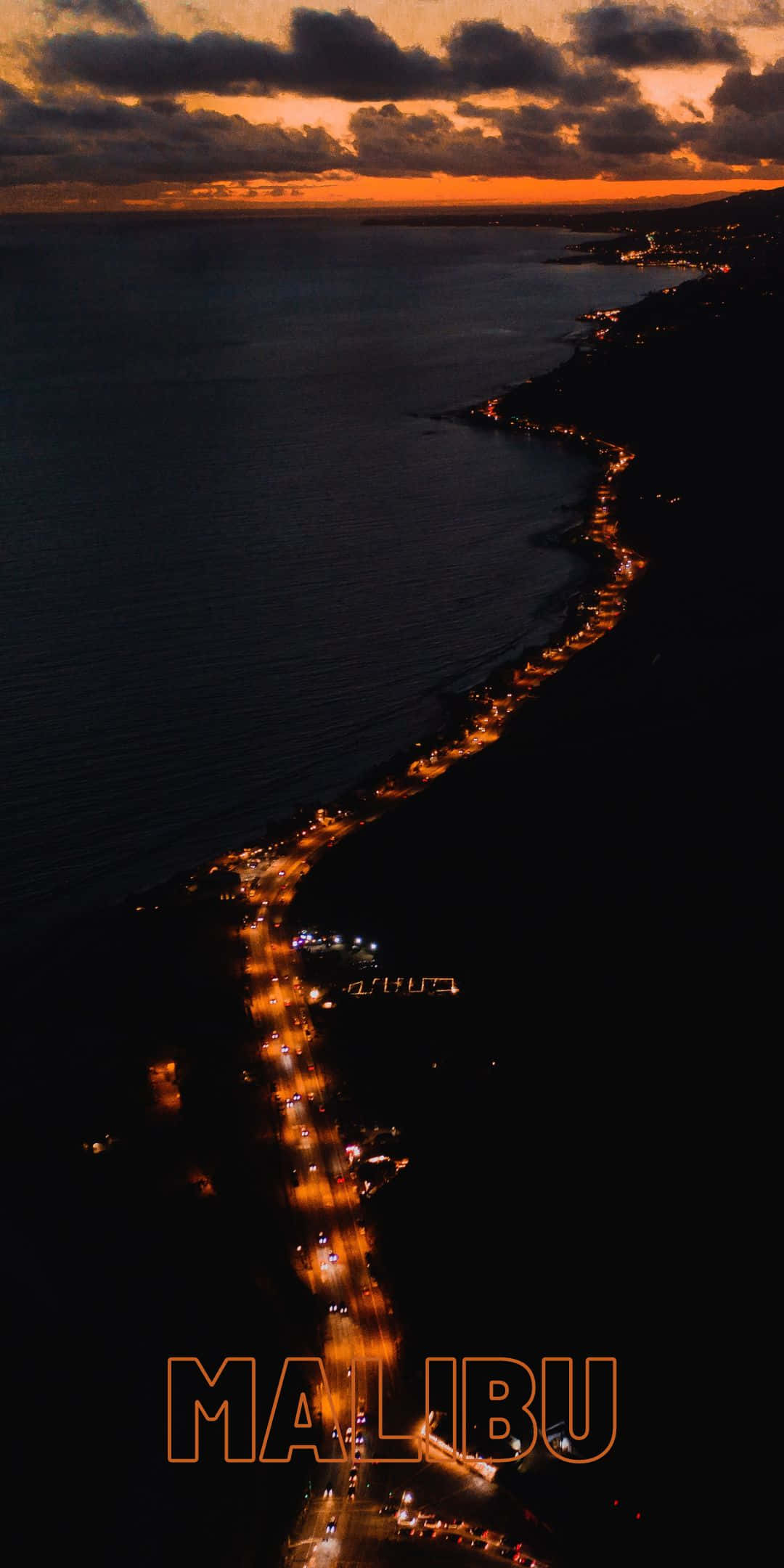 Road 桌布 壁紙 — 馬里布海岸線在黃昏時的鳥瞰圖，橙色雲層下，發光的道路燈光沿著黑暗的海岸蜿蜒而行。