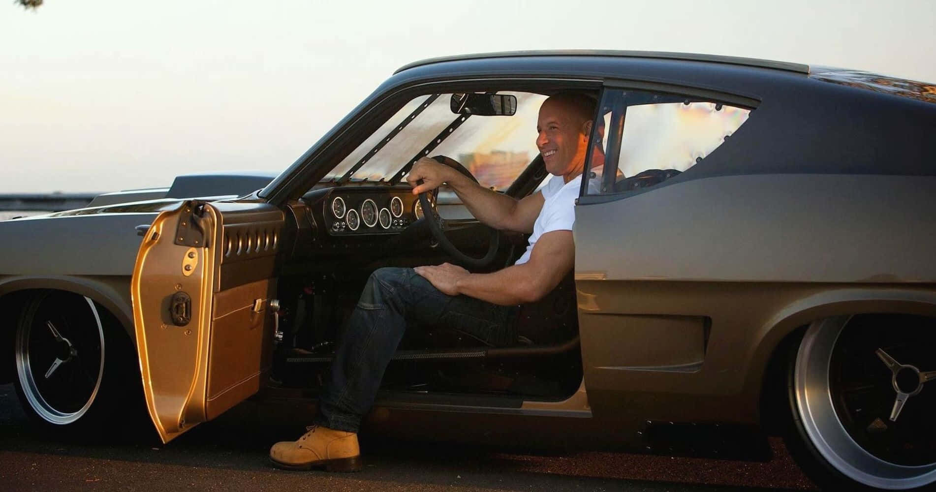 Fast And Furious 桌布 壁紙 — 馮·迪索在日落時坐在一輛訂製的肌肉車內，金色車門打開，微笑著。