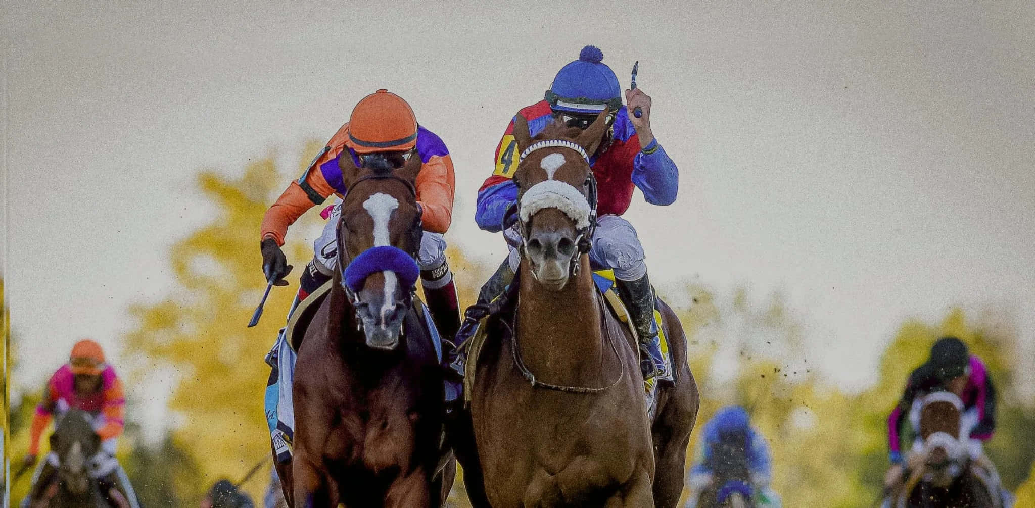 Preakness Horses 2022 桌布 壁紙 — 騎師穿著色彩繽紛的絲綢，高速競賽純種馬，背景有模糊的樹木。