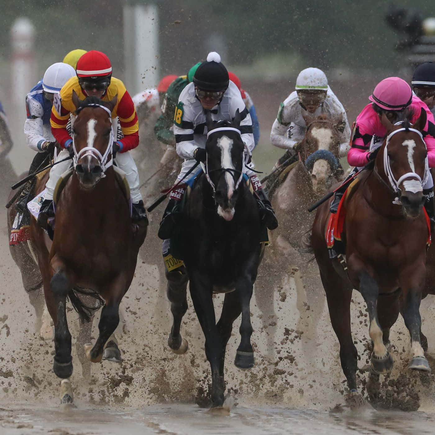 Kentucky Derby 桌布 壁紙 — 騎師身穿色彩繽紛的絲綢賽衣，策馬奔馳，濺起泥水，場面戲劇性十足。