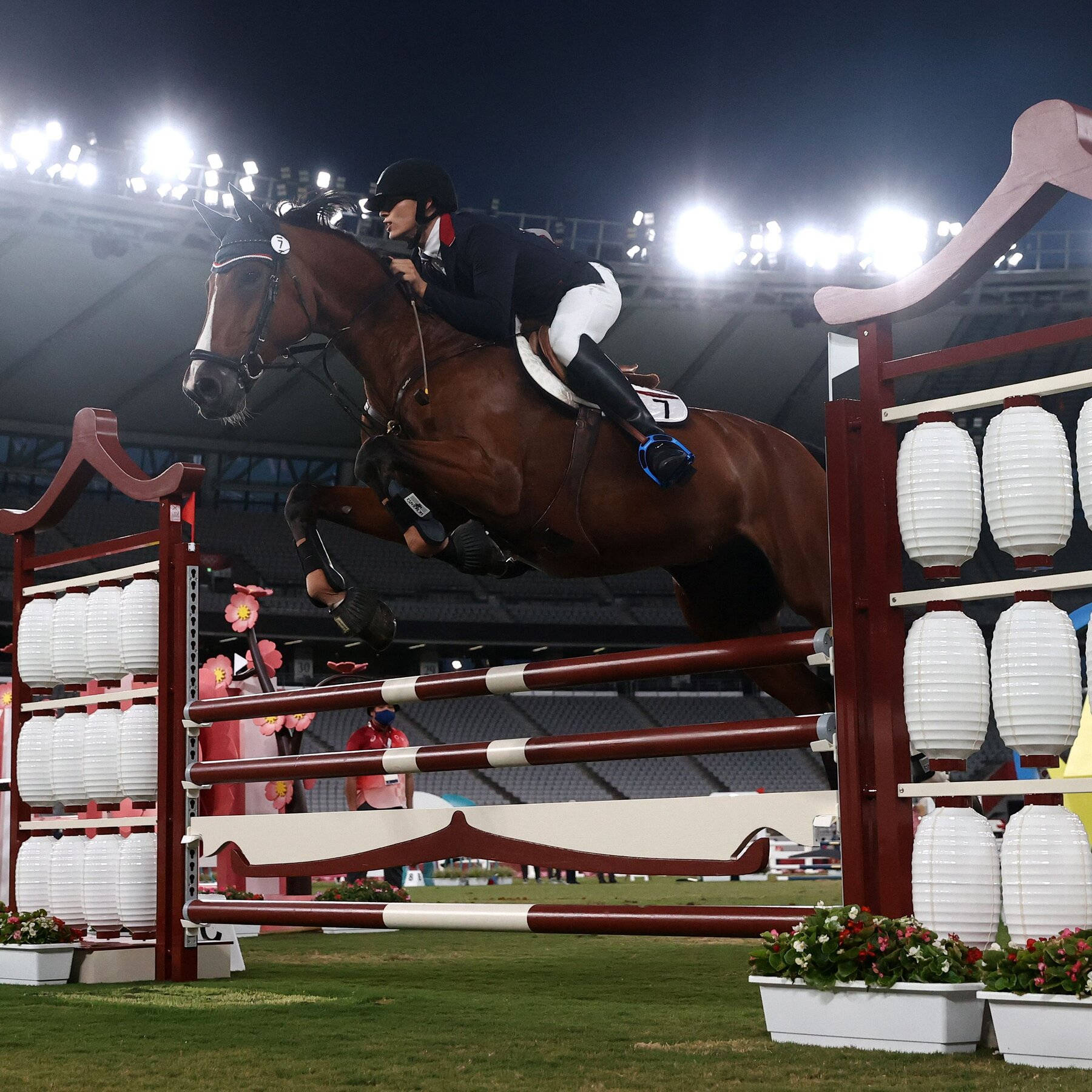 Athletic 桌布 壁紙 — 騎手和栗色馬在夜間明亮的體育場燈光下飛越裝飾性障礙物。