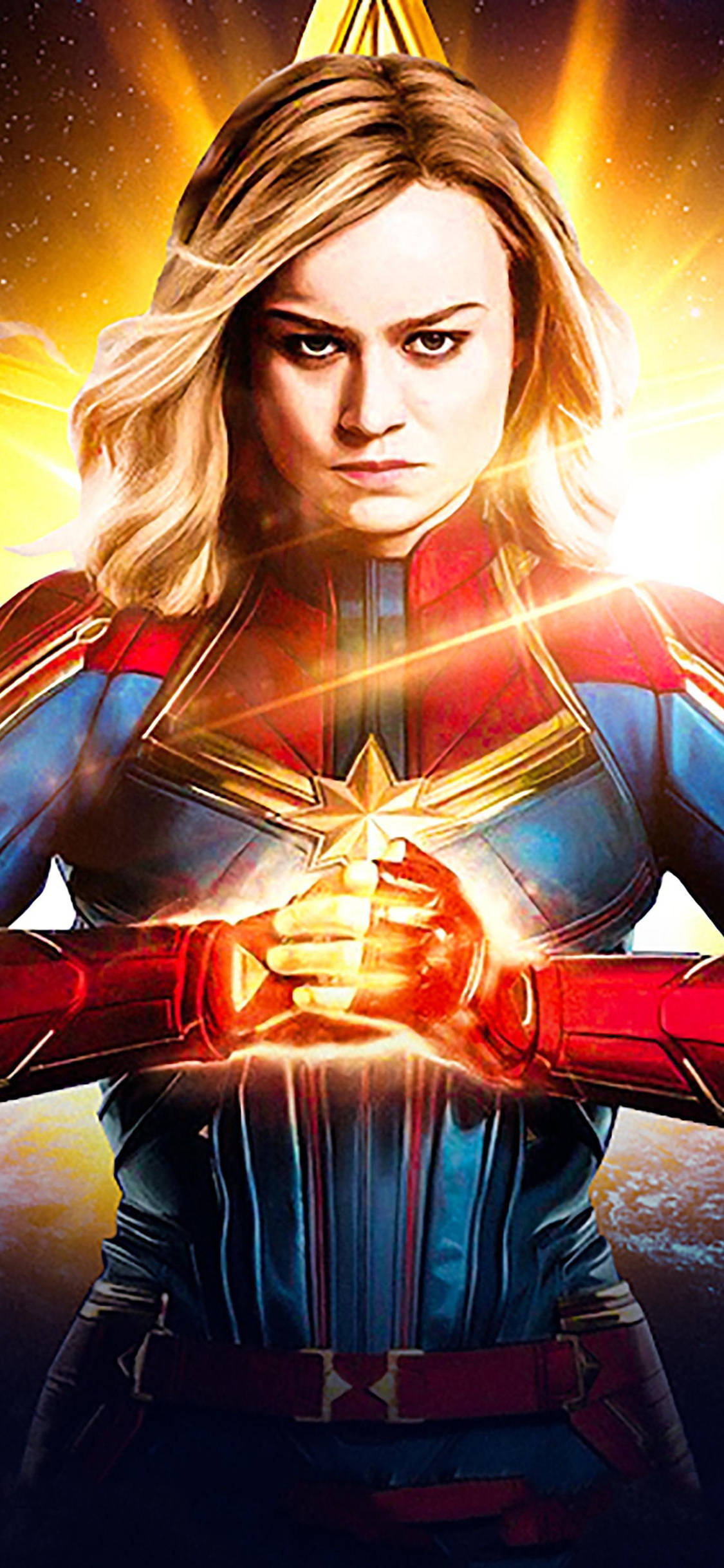 captain marvel iPhone 桌布 壁紙 — 驚奇隊長在宇宙場景中強勢站立，她穿著標誌性的紅、藍、金色戰衣，雙手散發出發光的能量。