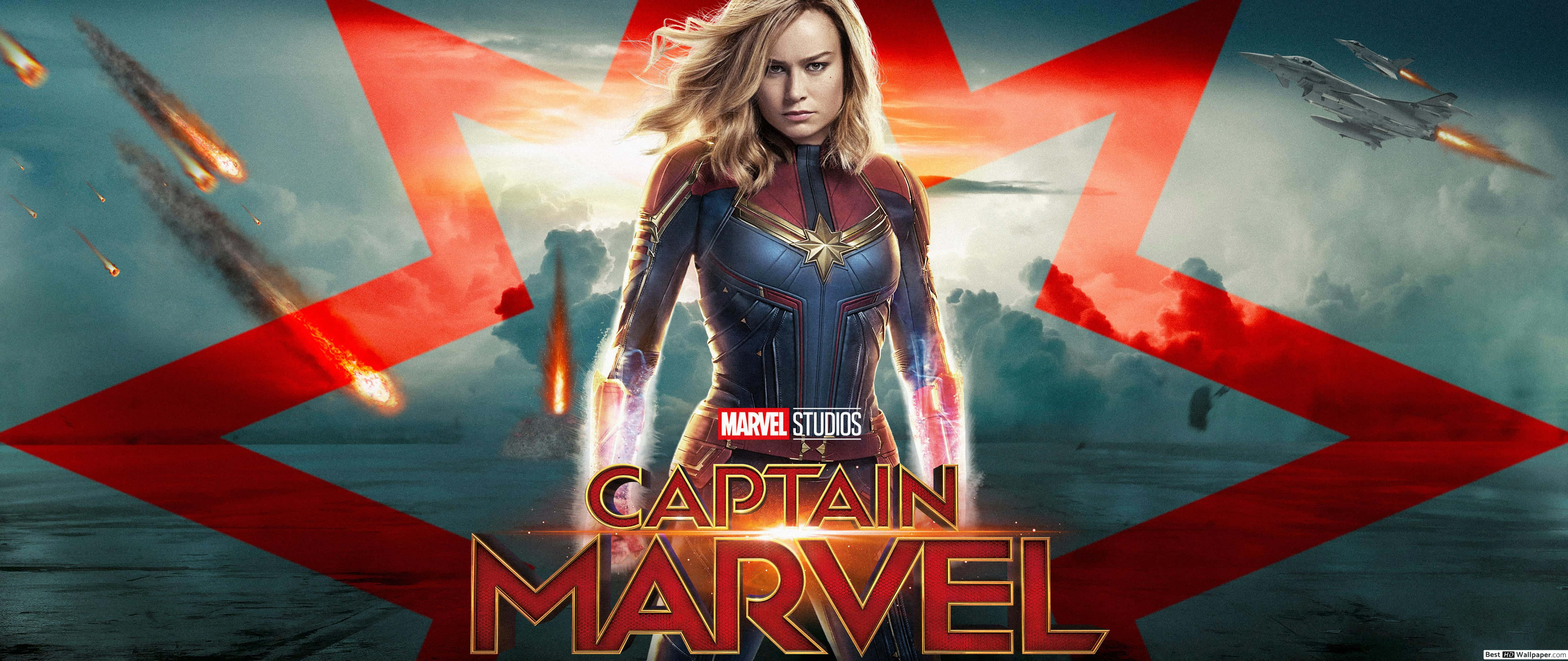 Captain Marvel 3d 桌布 壁紙 — 驚奇隊長在戲劇性的天空背景下，伴隨著紅色星爆和飛行的噴射機，在墜落的流星中英勇地站立。