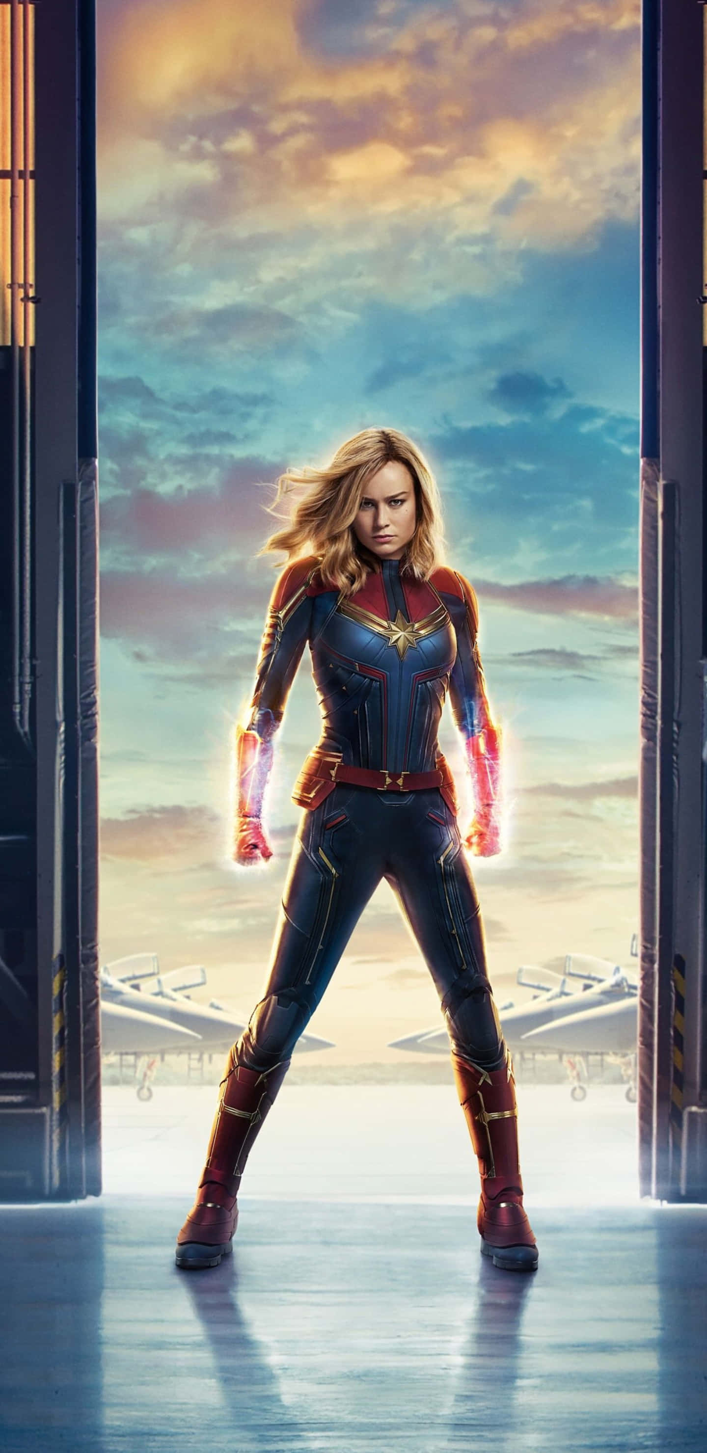 Pixel 3xl Captain Marvel 桌布 壁紙 — 驚奇隊長在未來風格的門口強勢站立，雙手發光，背景是充滿活力的日落天空。