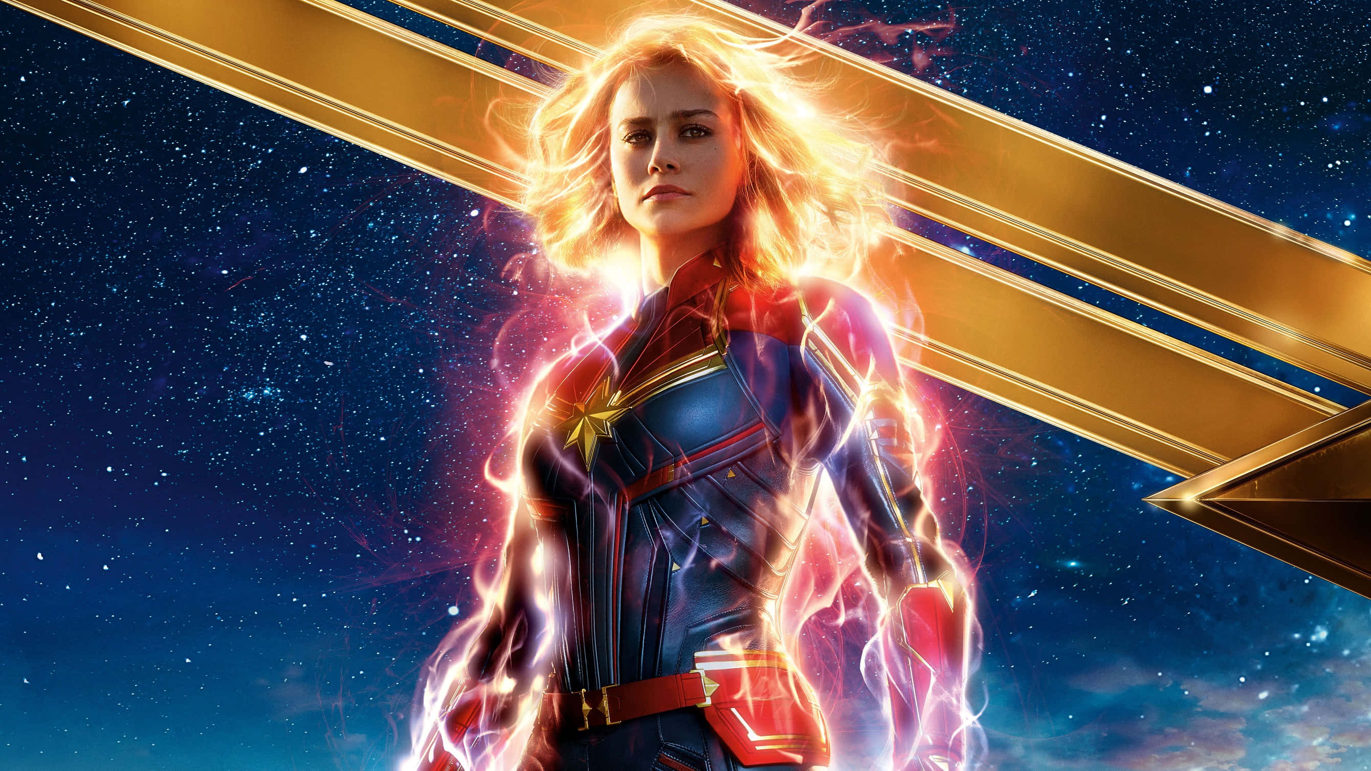 Captain Marvel 桌布 壁紙 — 驚奇隊長在繁星點點的宇宙背景下強勢站立，金色能量在她周圍噼啪作響。