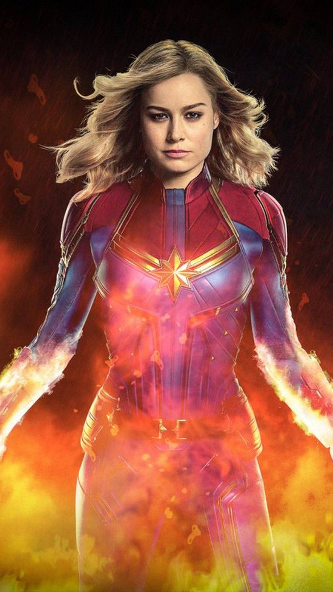 captain marvel iPhone 桌布 壁紙 — 驚奇隊長在黑暗背景下，雙手散發出熾熱能量，強勢地站立於火焰光環之中。