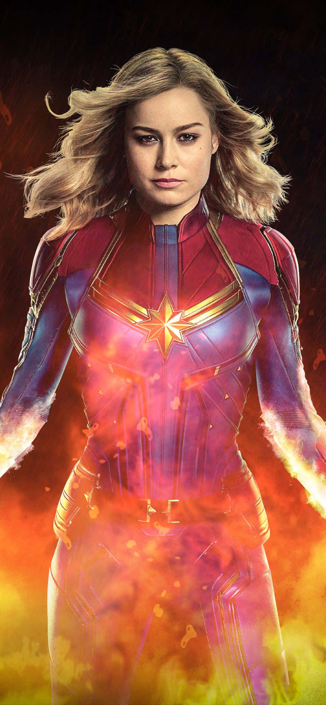captain marvel iPhone 桌布 壁紙 — 驚奇隊長強大地站在一個發光的宇宙能量場中，熾熱的橙色和紫色色調在她周圍旋轉。