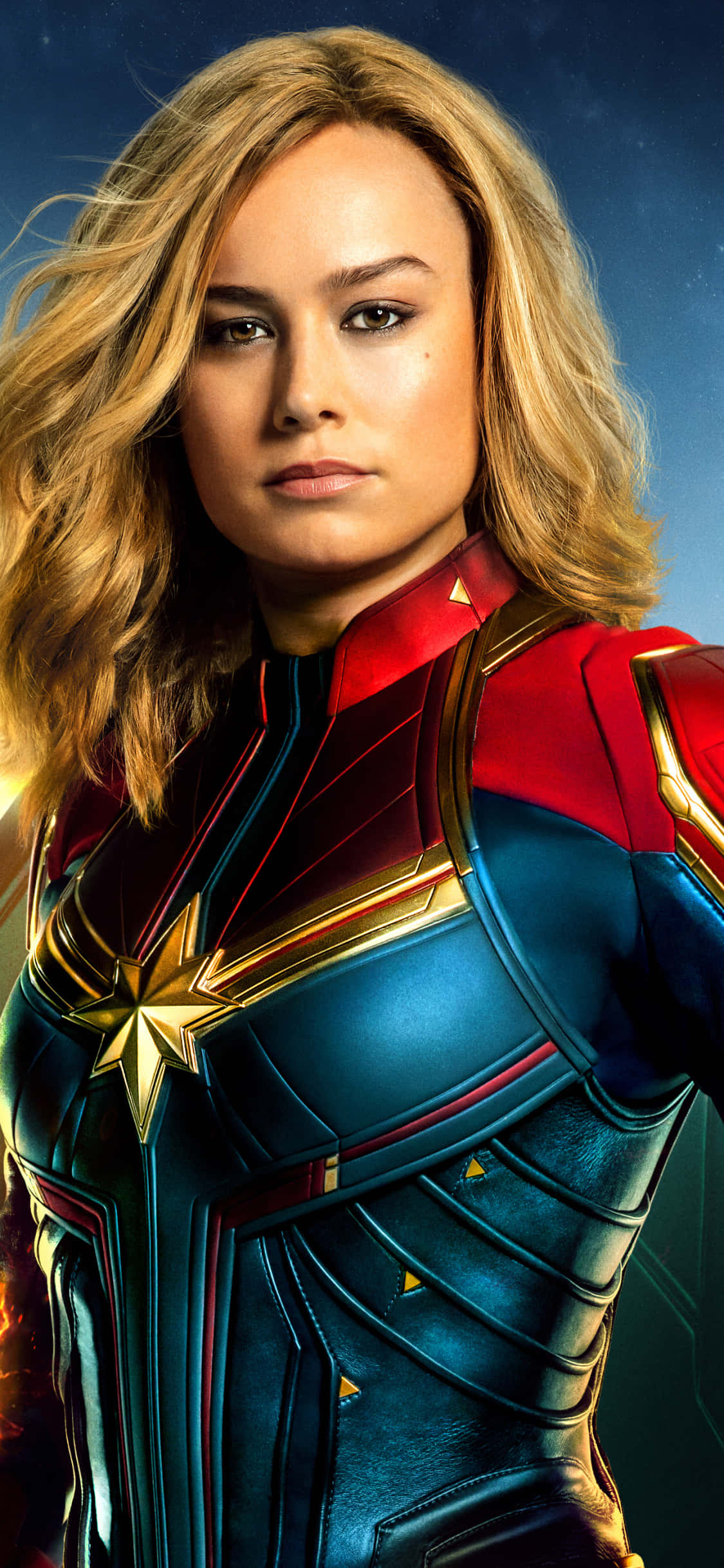 brie larson 桌布 壁紙 — 驚奇隊長自信地穿著她標誌性的紅藍金戰衣，站在宇宙星空背景前。