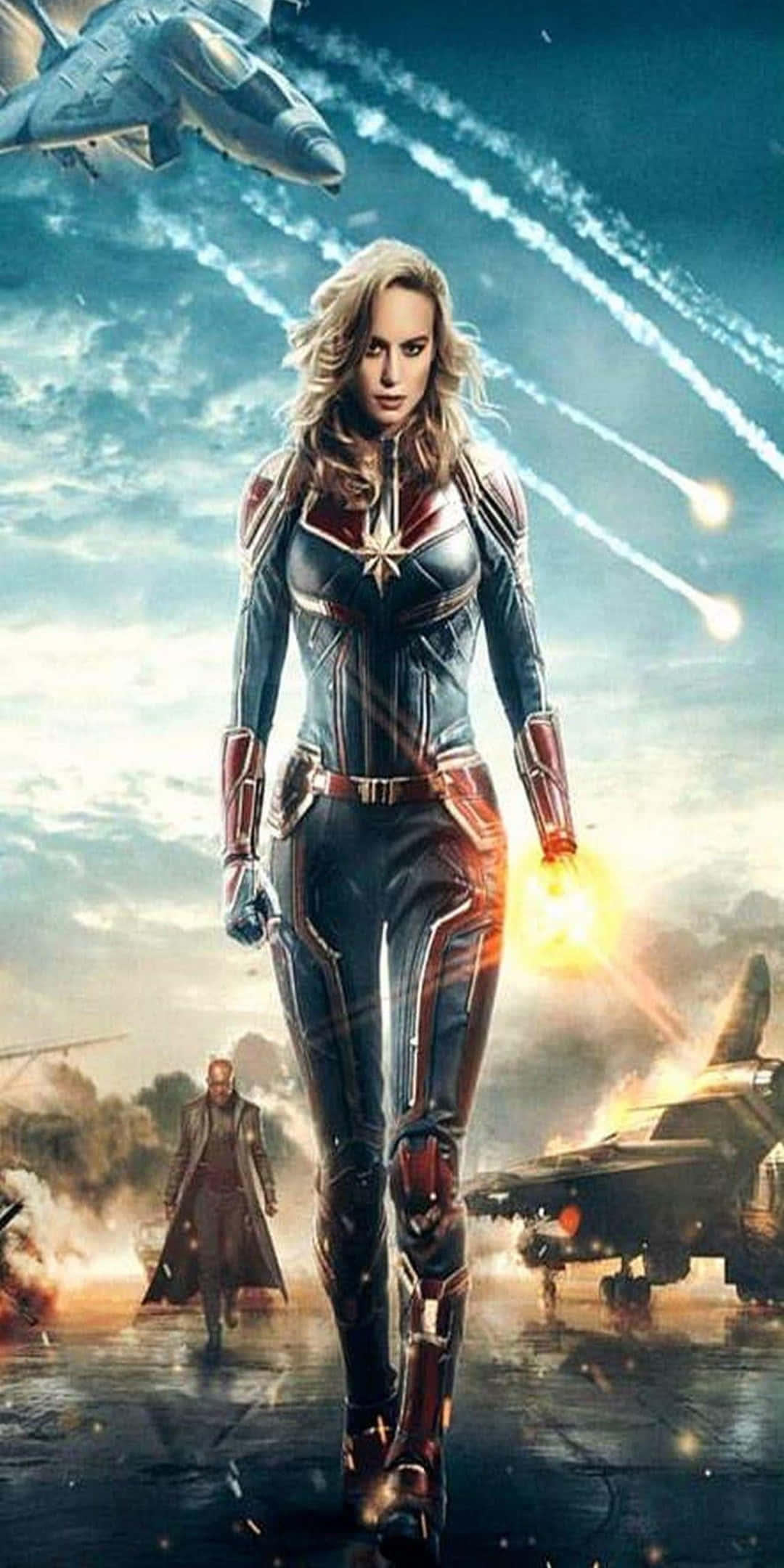 Captain Marvel 桌布 壁紙 — 驚奇隊長自信地穿著她的星條旗戰衣，站在戰鬥機和爆炸背景的戰場上。