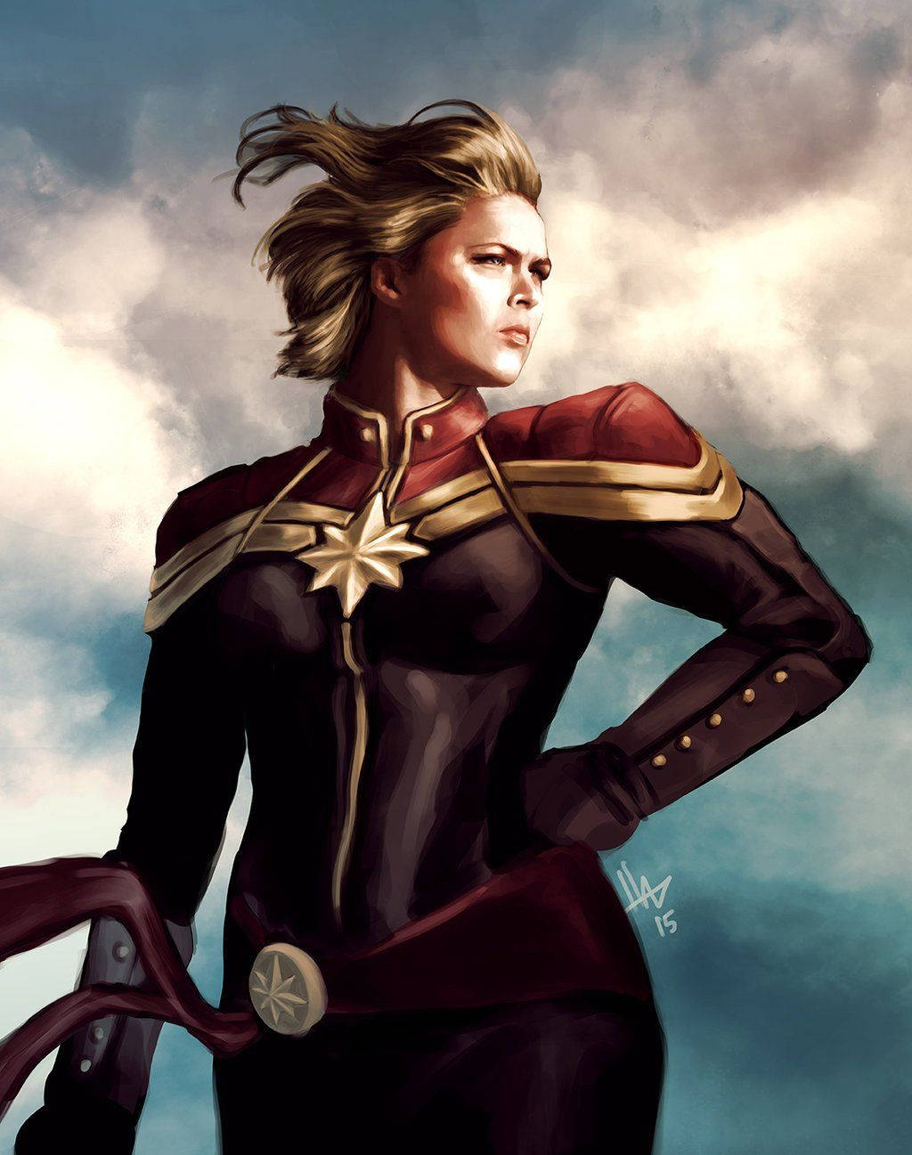Captain Marvel 桌布 壁紙 — 驚奇隊長自信地站在多雲的天空下，穿著她標誌性的紅金和深色服裝，帶有星星標誌。