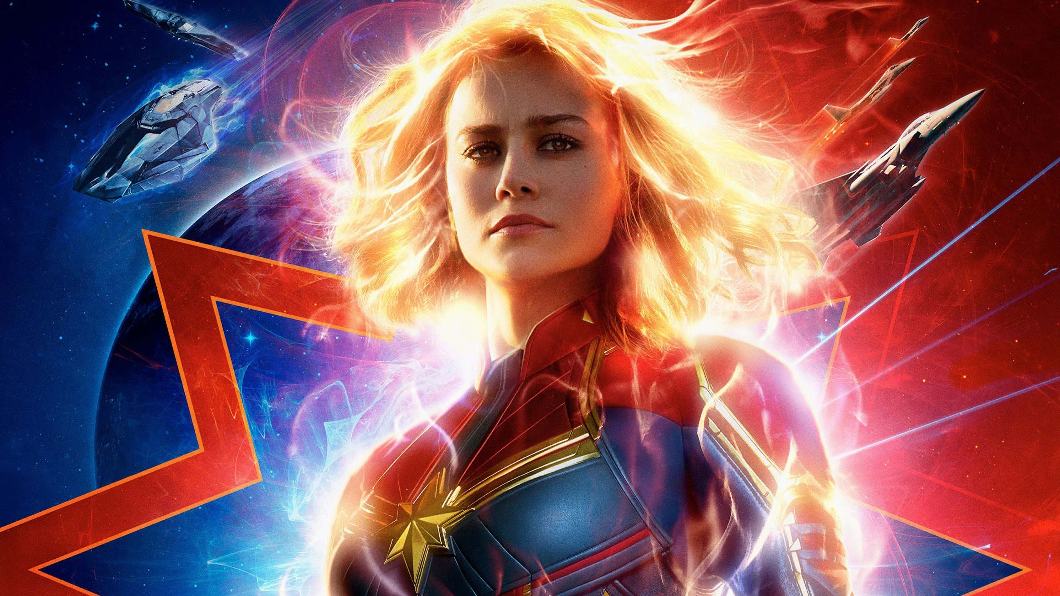 Captain Marvel 桌布 壁紙 — 驚奇隊長英勇地站在太空中，散發出光芒四射的能量，周圍是未來風格的太空船和充滿活力的宇宙背景。