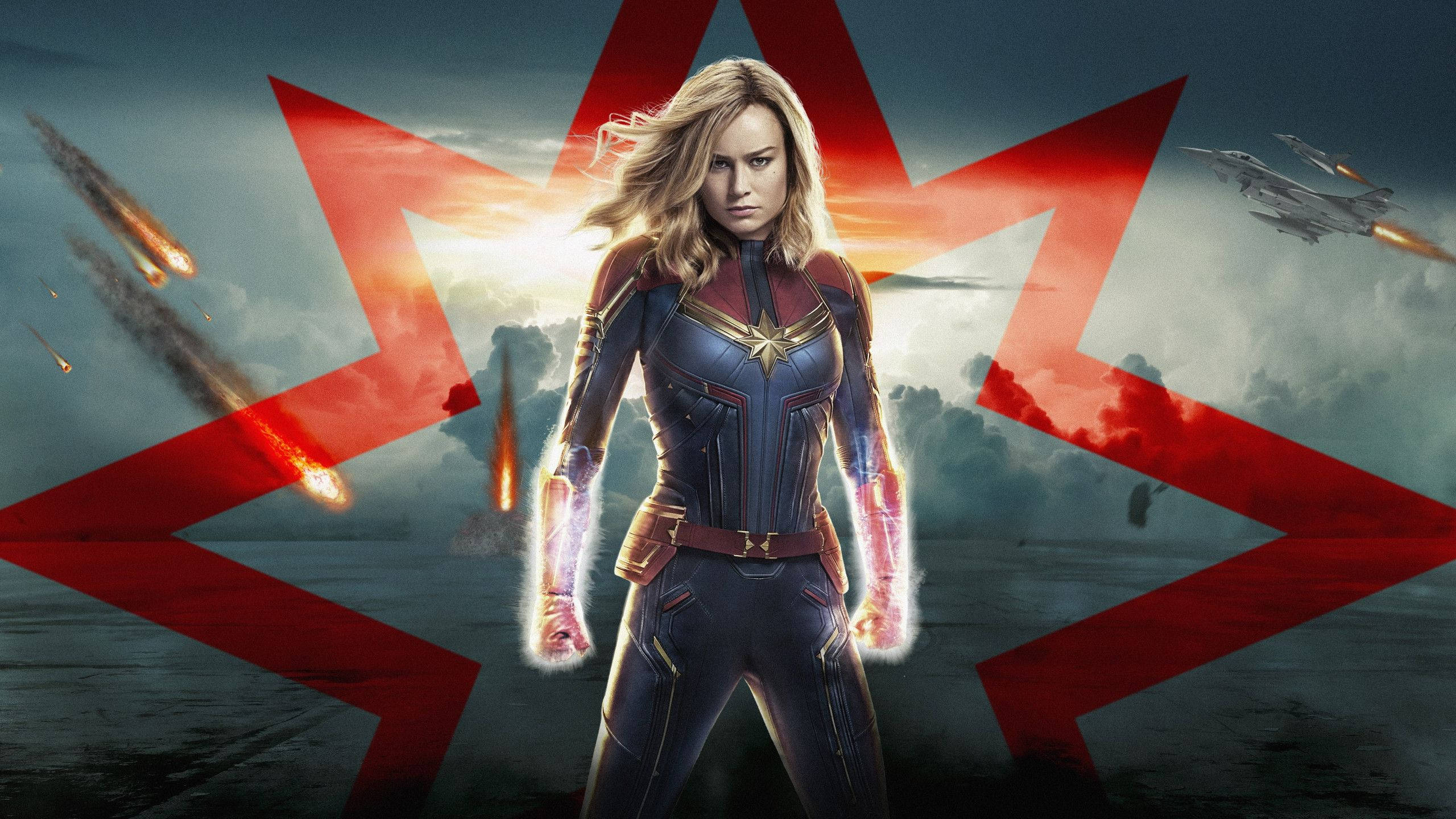 brie larson 桌布 壁紙 — 驚奇隊長英勇地站在戲劇性的天空下，流星劃過，戰鬥機圍繞著大膽的紅星飛行。