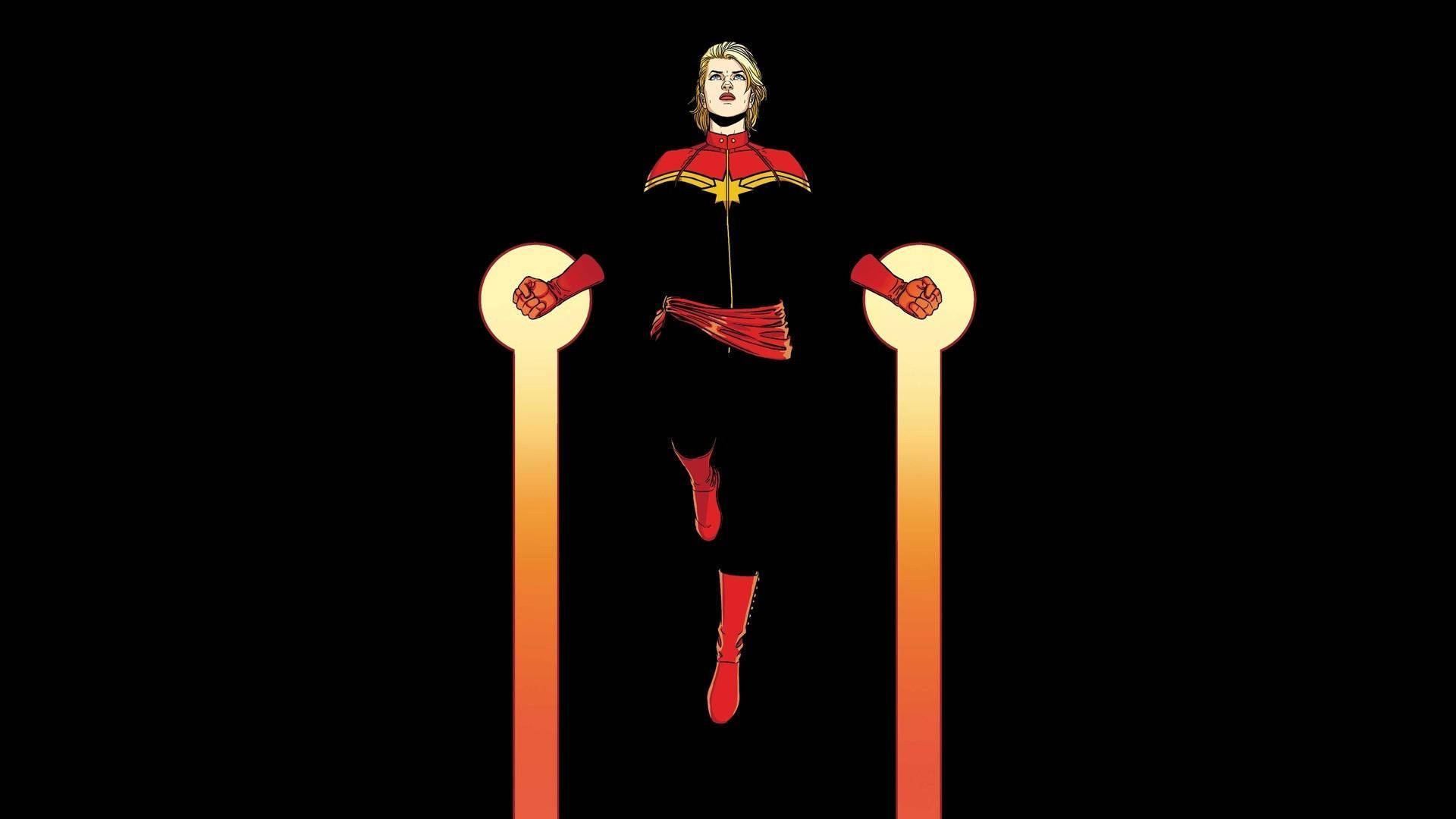 captain marvel 4K 桌布 壁紙 — 驚奇隊長英勇地站在黑色背景前兩根發光的橙色柱子之間。