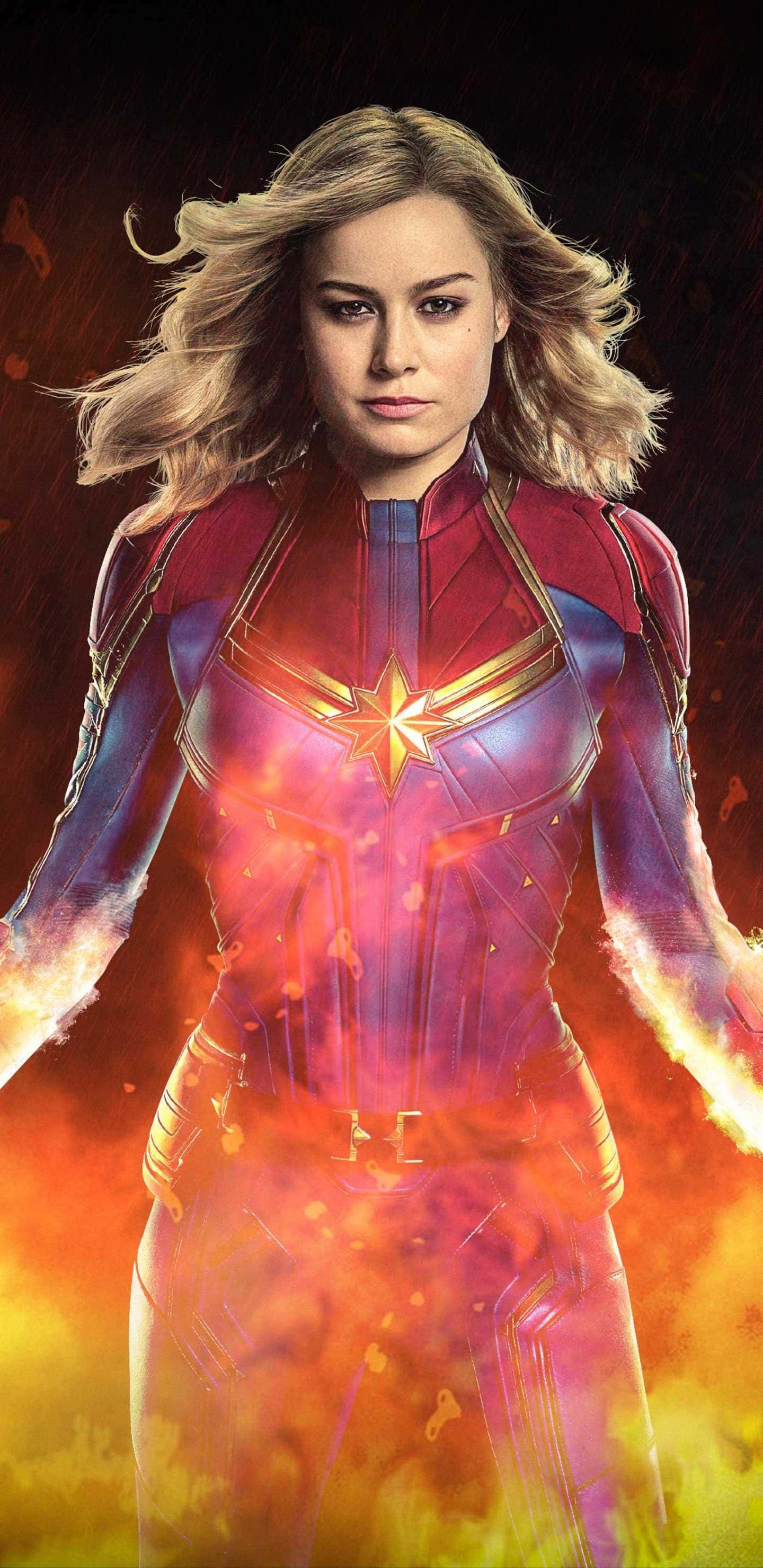 Captain Marvel 桌布 壁紙 — 驚奇隊長身穿發光的宇宙戰衣，在熾熱星雲背景下強勢站立。