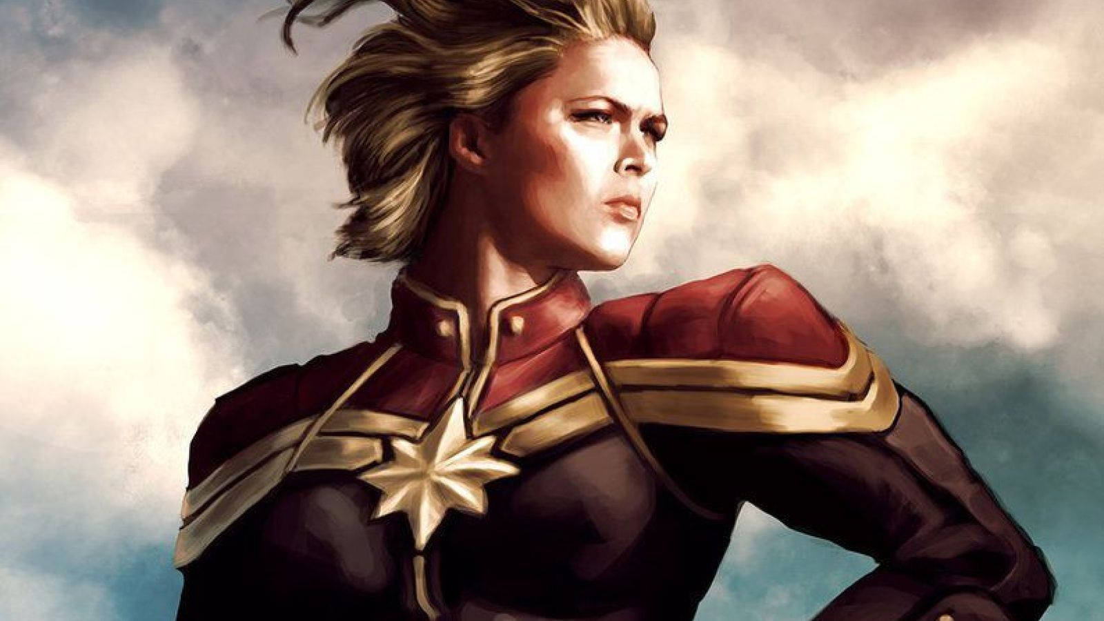 Captain Marvel 桌布 壁紙 — 驚奇隊長身穿紅金戰衣，在戲劇性的多雲天空下堅定站立，風吹動她的金髮。