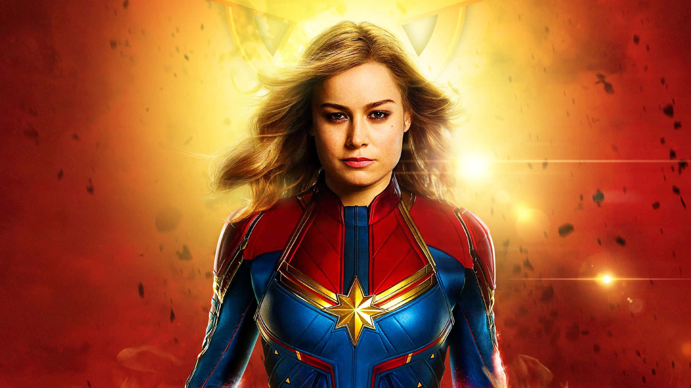 Captain Marvel 桌布 壁紙 — 驚奇隊長身穿藍紅戰衣，胸前閃耀星星標誌，在熾熱的橙紅色宇宙背景下英勇站立。