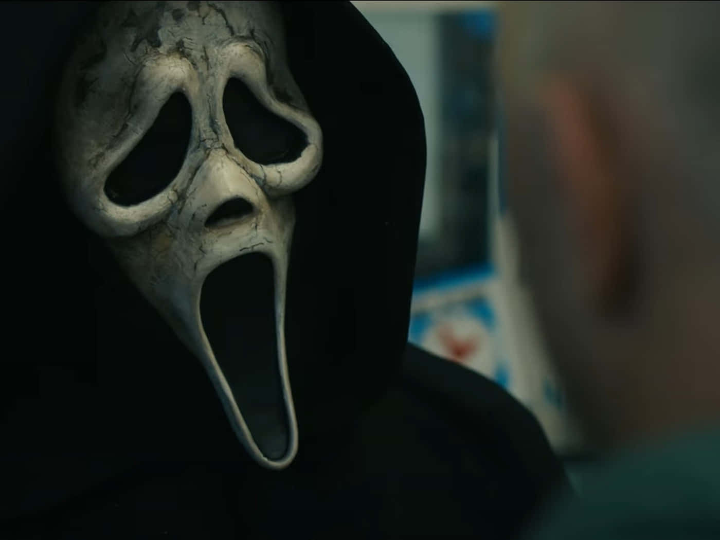 鬼臉殺手 桌布 壁紙 — 《驚聲尖叫》中標誌性白色Ghostface面具的特寫，帶有裂紋質感和黑色連帽，面向昏暗燈光下模糊的人影。