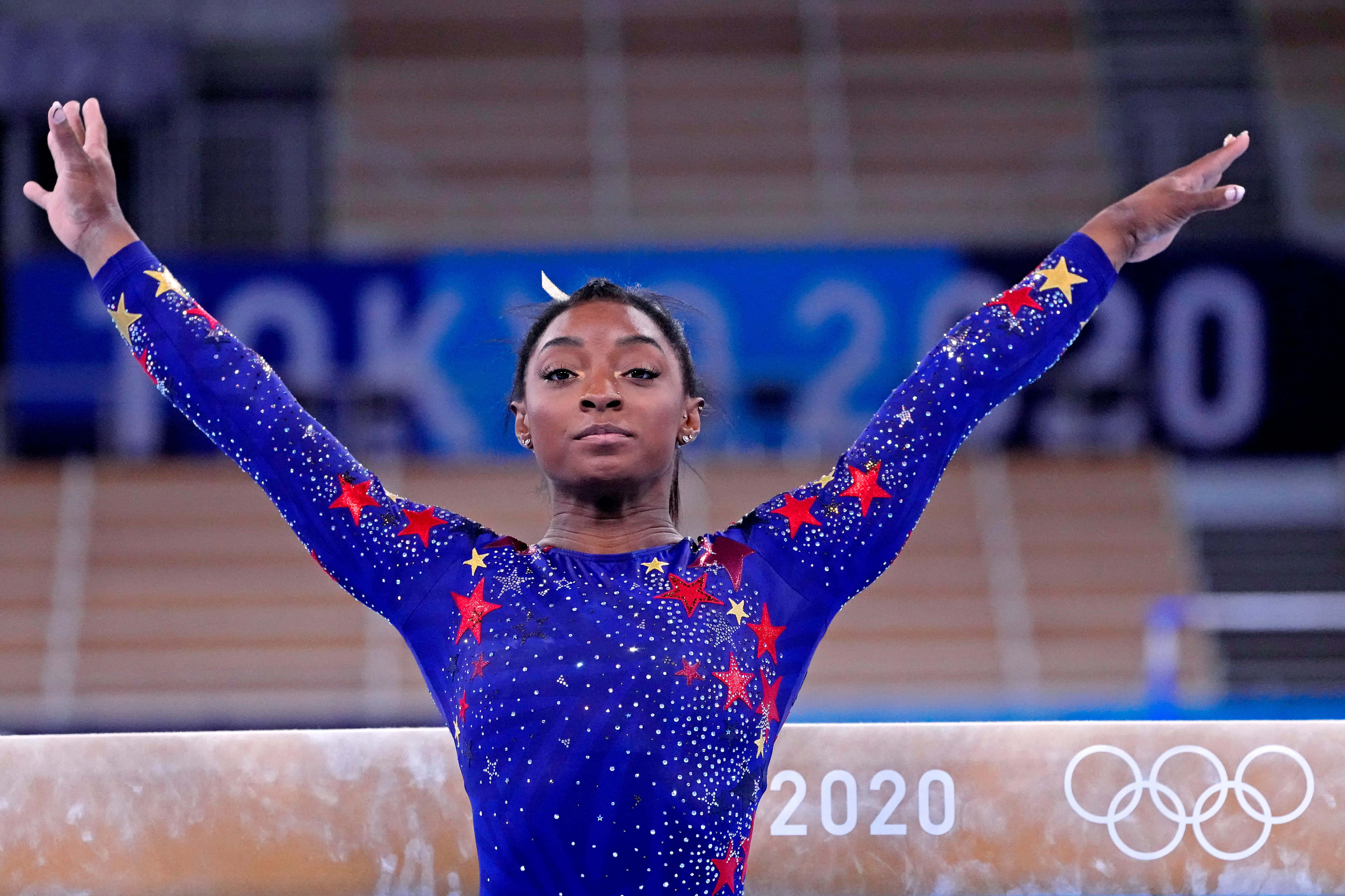 體操 桌布 壁紙 — 體操運動員Simone Biles身穿藍色星條緊身衣，在2020年東京奧運會的平衡木上高舉雙臂，勝利姿態。