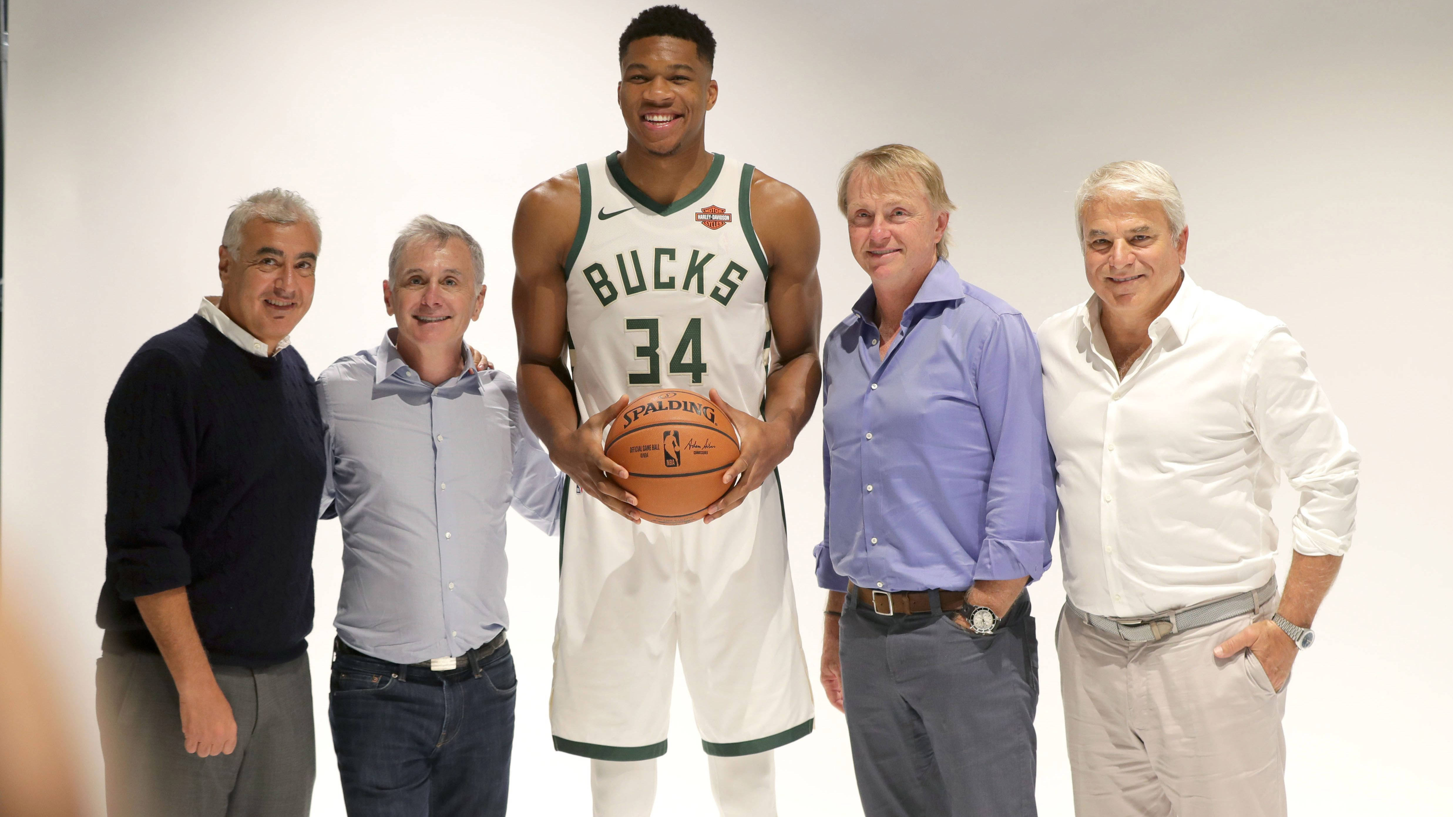 Giannis 桌布 壁紙 — 高大的籃球運動員身穿公鹿隊球衣，手持Spalding籃球，與四位微笑的男子在純白背景前擺姿勢。