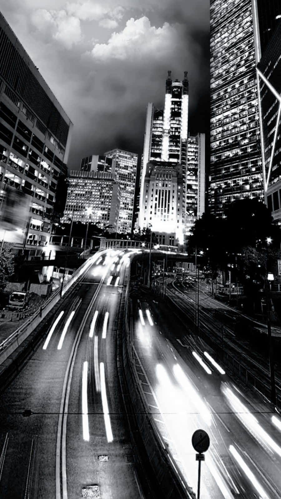 Black And White iPhone 桌布 壁紙 — 高對比度的黑白城市夜景，車流燈光在高聳摩天大樓下流動形成光軌。