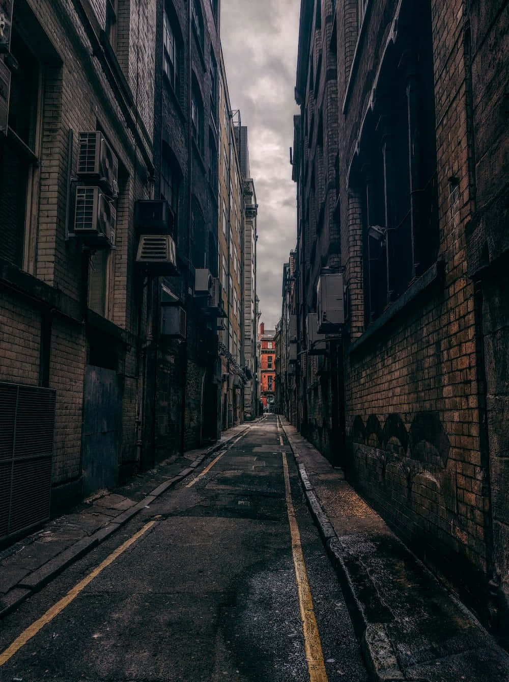 Dark Alleyway 桌布 壁紙 — 高樓磚建築之間一條狹窄的城市小巷，陰天，黃色道路標線。
