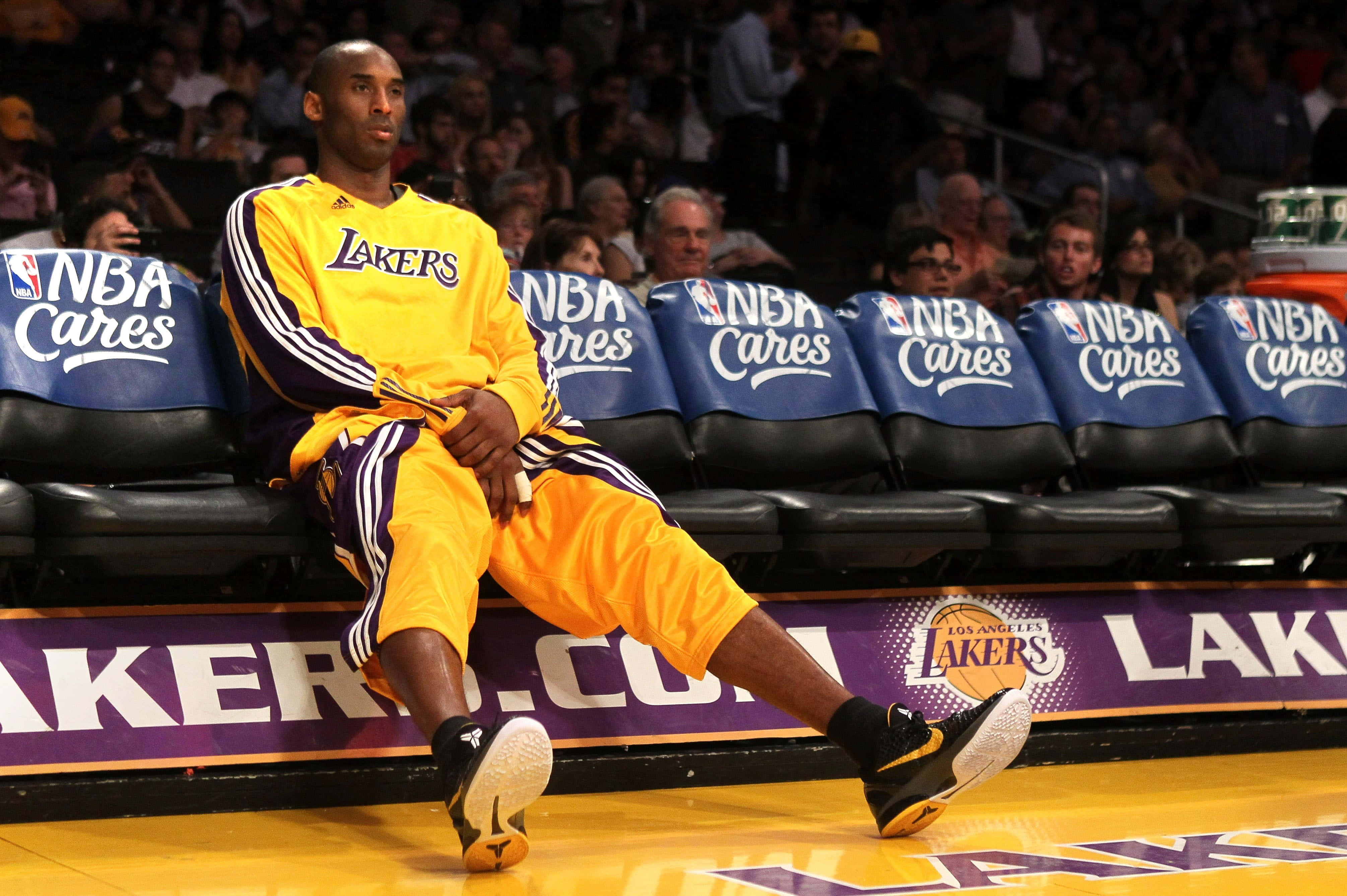 NBA 桌布 壁紙 — 高比拜仁穿著黃色湖人熱身服，在籃球比賽期間隨意坐在板凳上，背景有觀眾。