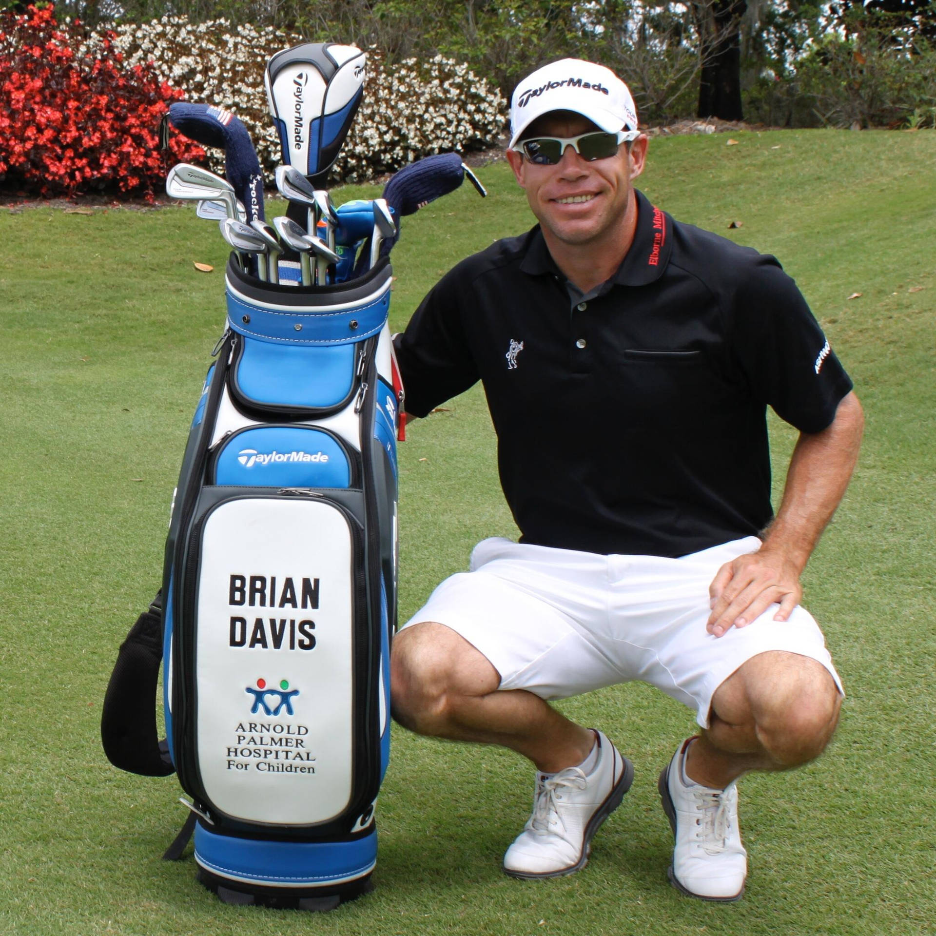  壁紙 — 高爾夫球手 Brian Davis 在翠綠的高爾夫球場上蹲在其品牌 TaylorMade 球袋旁微笑。