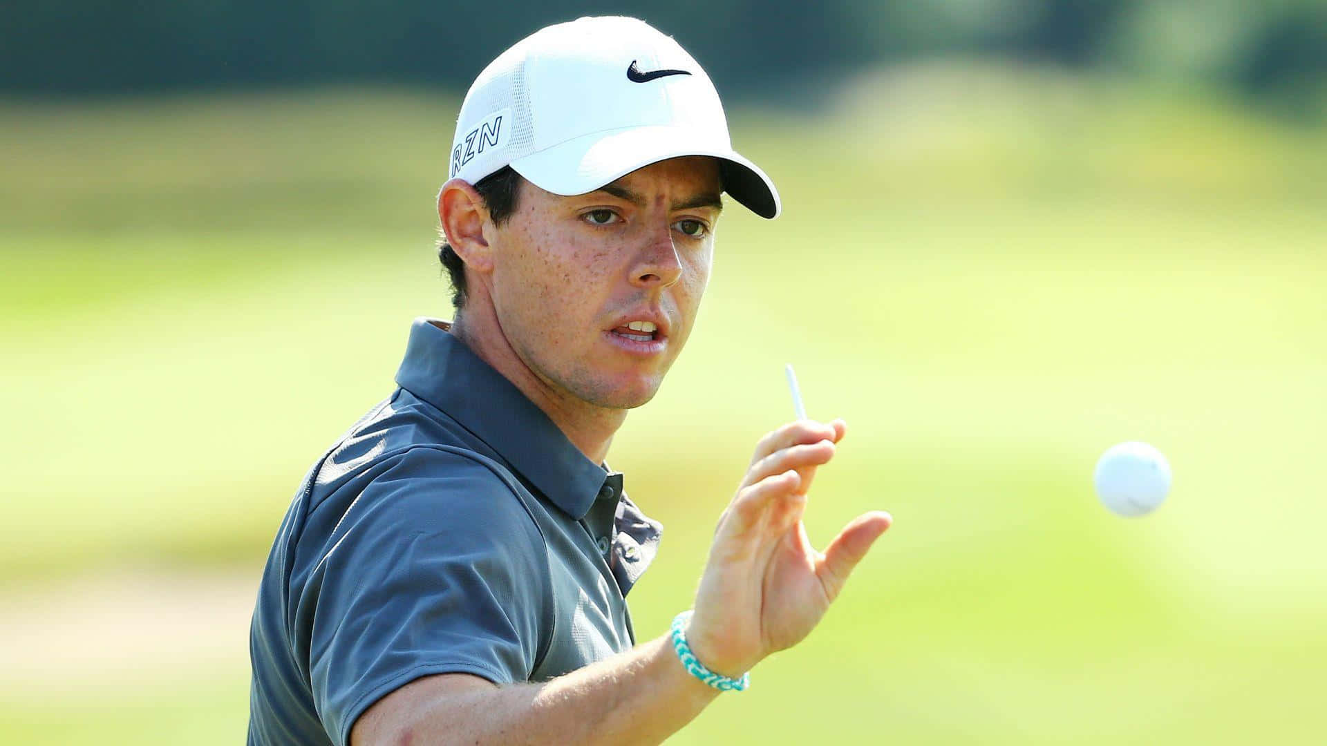 高爾夫 桌布 壁紙 — 高爾夫球手Rory McIlroy在陽光明媚的高爾夫球場上揮桿，背景是模糊的綠色。