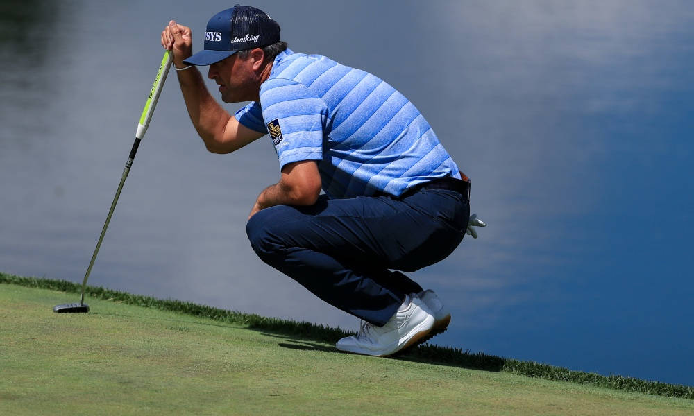 Ryan Palmer 桌布 壁紙 — 高爾夫球手在平靜的藍色水邊的綠色草地上專注地蹲下，握著推桿。