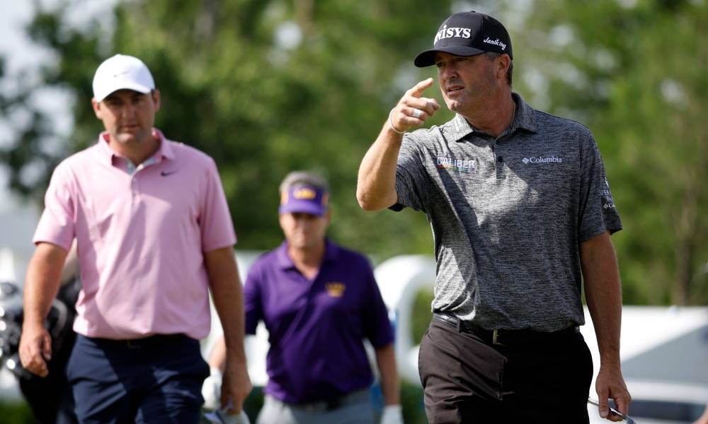 Ryan Palmer 桌布 壁紙 — 高爾夫球手在陽光明媚的球場上行走，一人興奮地指點，另一人則穿過茂密的綠樹攜帶球桿。