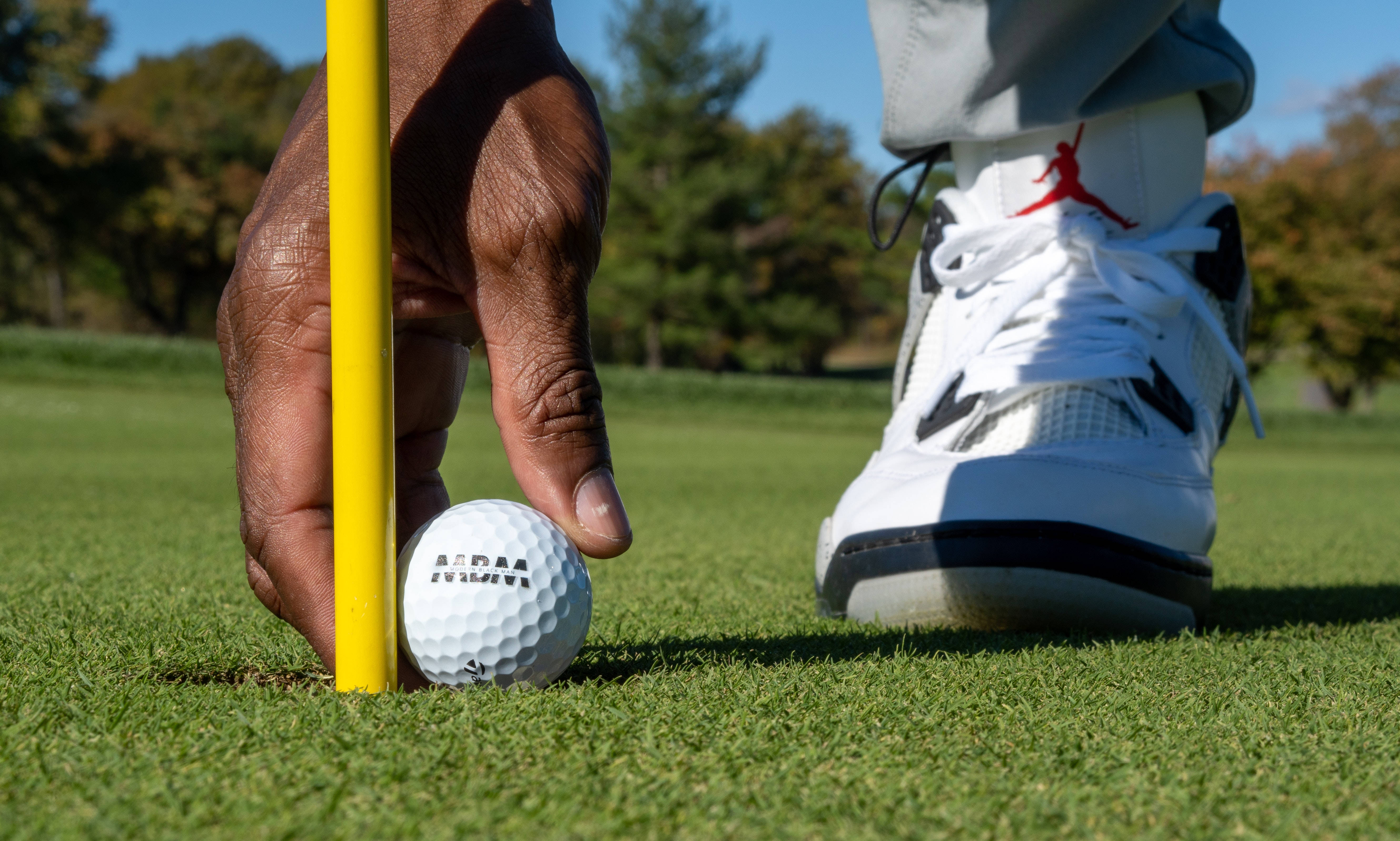 4K Golf 桌布 壁紙 — 高爾夫球手的手引導一個白色高爾夫球靠近洞口，而一雙帶有紅色標誌的白色運動鞋則準備好在充滿活力的綠色草地上。