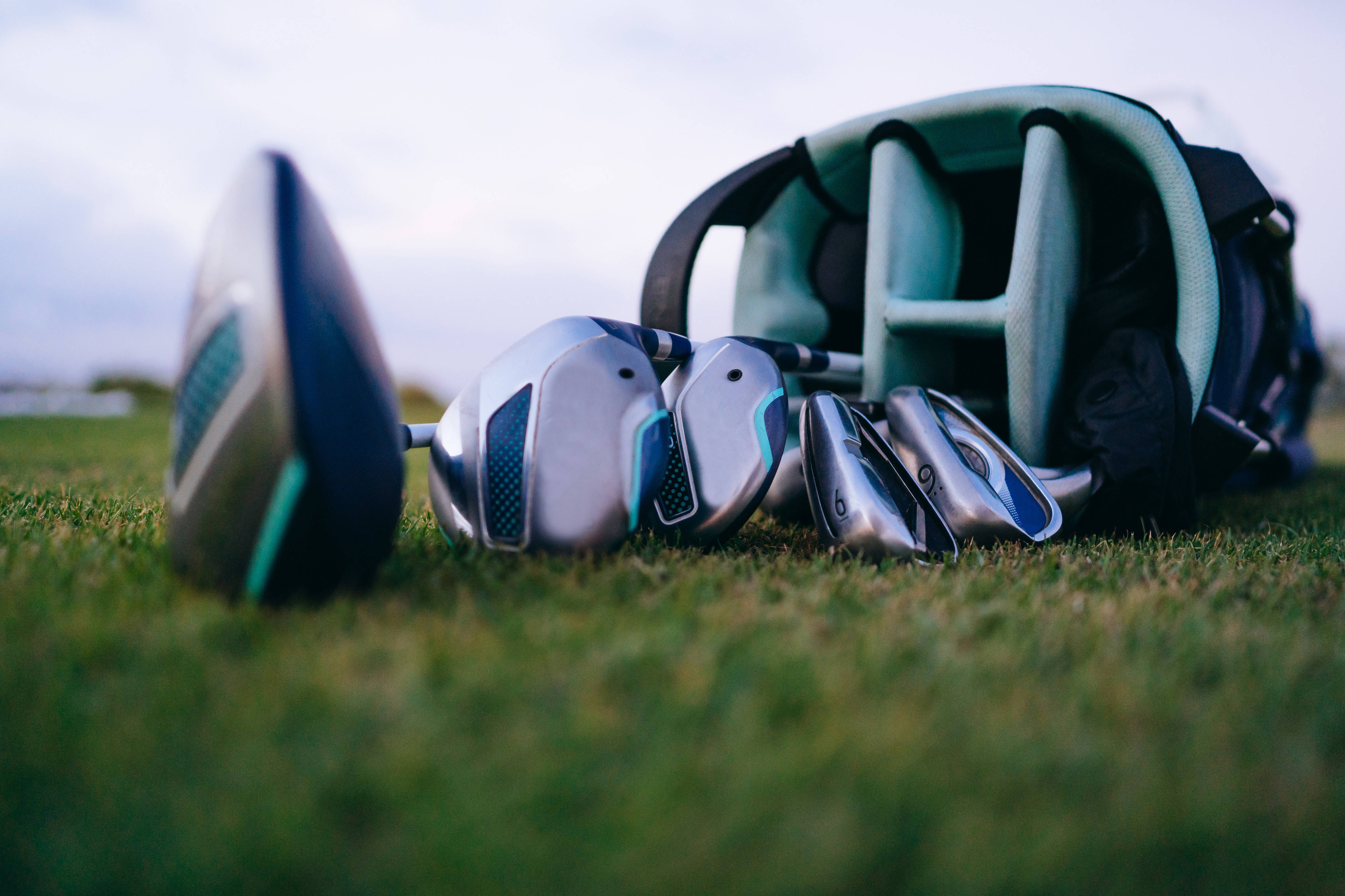 4K Golf 桌布 壁紙 — 高爾夫球桿和球袋放在茂密的綠草地上，背景是柔和的多雲天空，景深較淺。