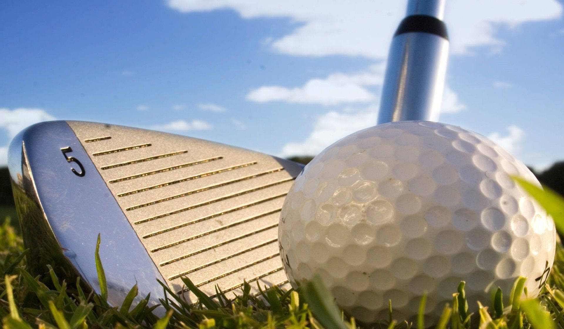 Golfing 桌布 壁紙 — 高爾夫球桿和高爾夫球在鮮綠色草地上的特寫，背景是明亮的藍天和零星白雲。
