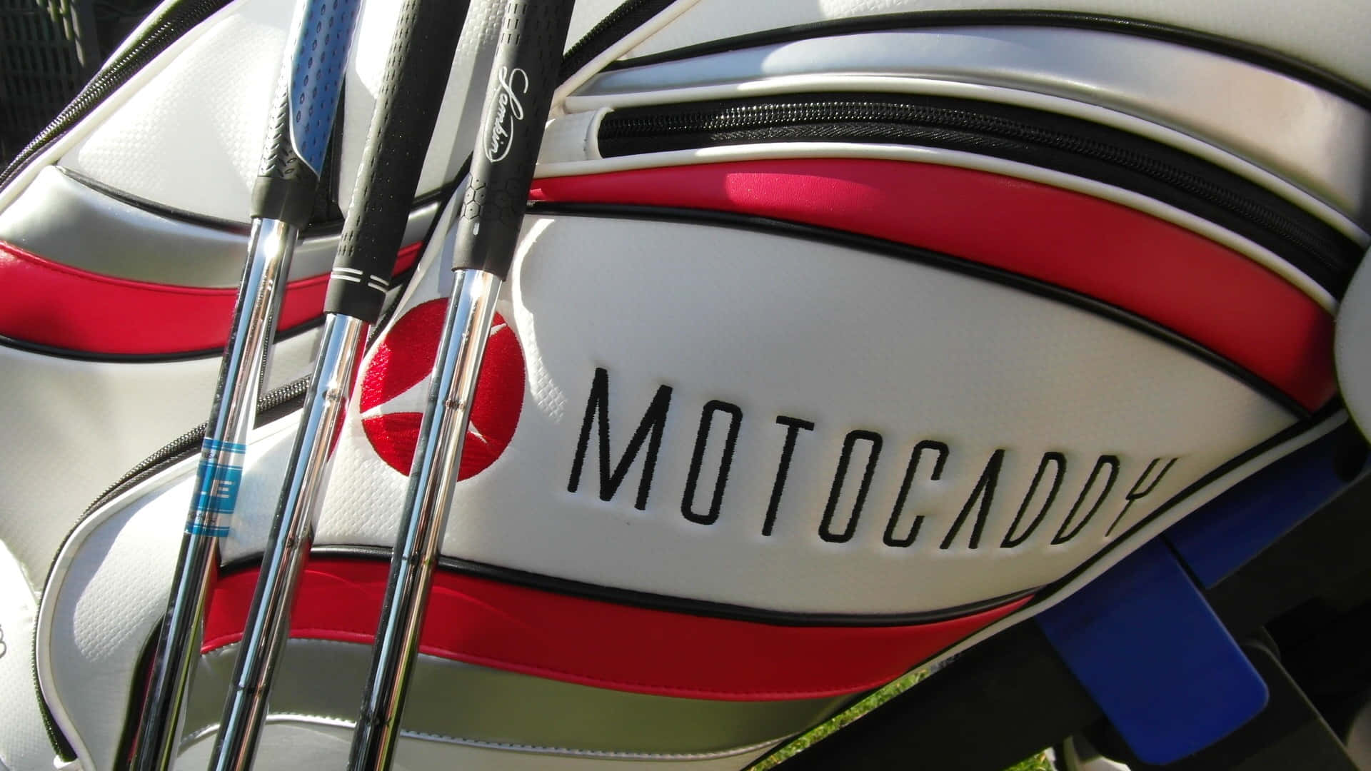 Golf Club 桌布 壁紙 — 高爾夫球桿從白色、紅色和黑色的 Motocaddy 高爾夫球袋中露出的特寫，在明亮的陽光下。