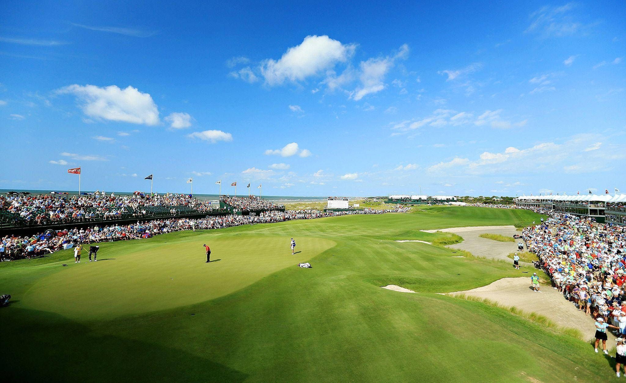 Pga 桌布 壁紙 — 高空俯瞰一個充滿活力的綠色高爾夫球場，上方是明亮的藍天，散落著白雲，觀眾看台座無虛席。