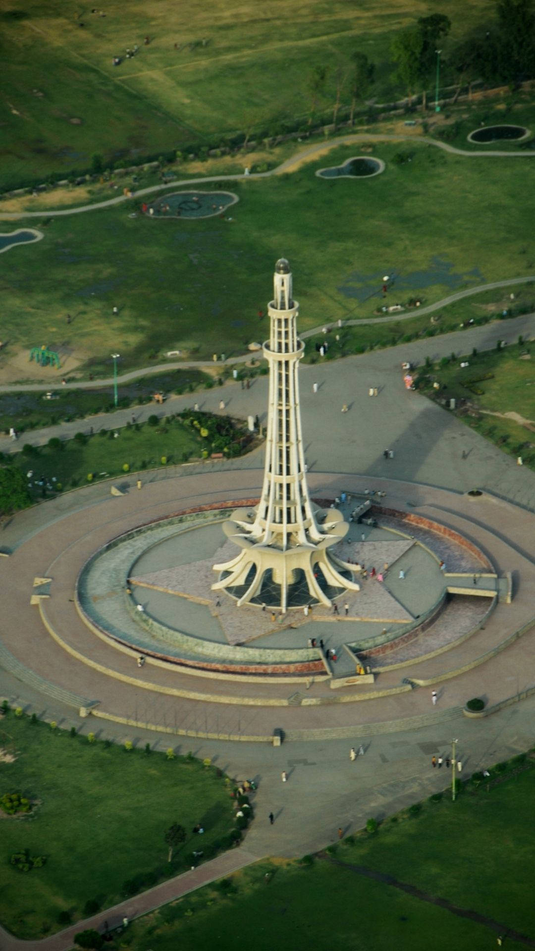 Pakistan 桌布 壁紙 — 高空俯瞰一座高聳的白色塔樓紀念碑，周圍環繞著圓形步道和鬱鬱蔥蔥的公園綠地，散落著遊客。