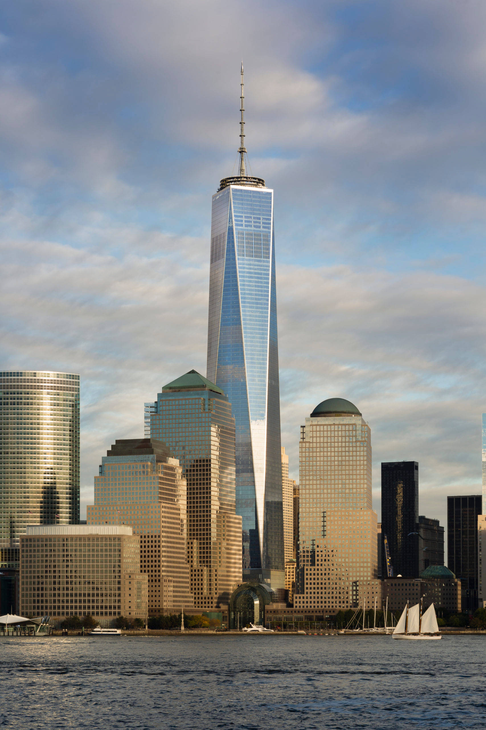 日出 桌布 壁紙 — 高聳入雲的One World Trade Center倒映著紐約市天際線上的藍天白雲，下方水面有帆船點綴。