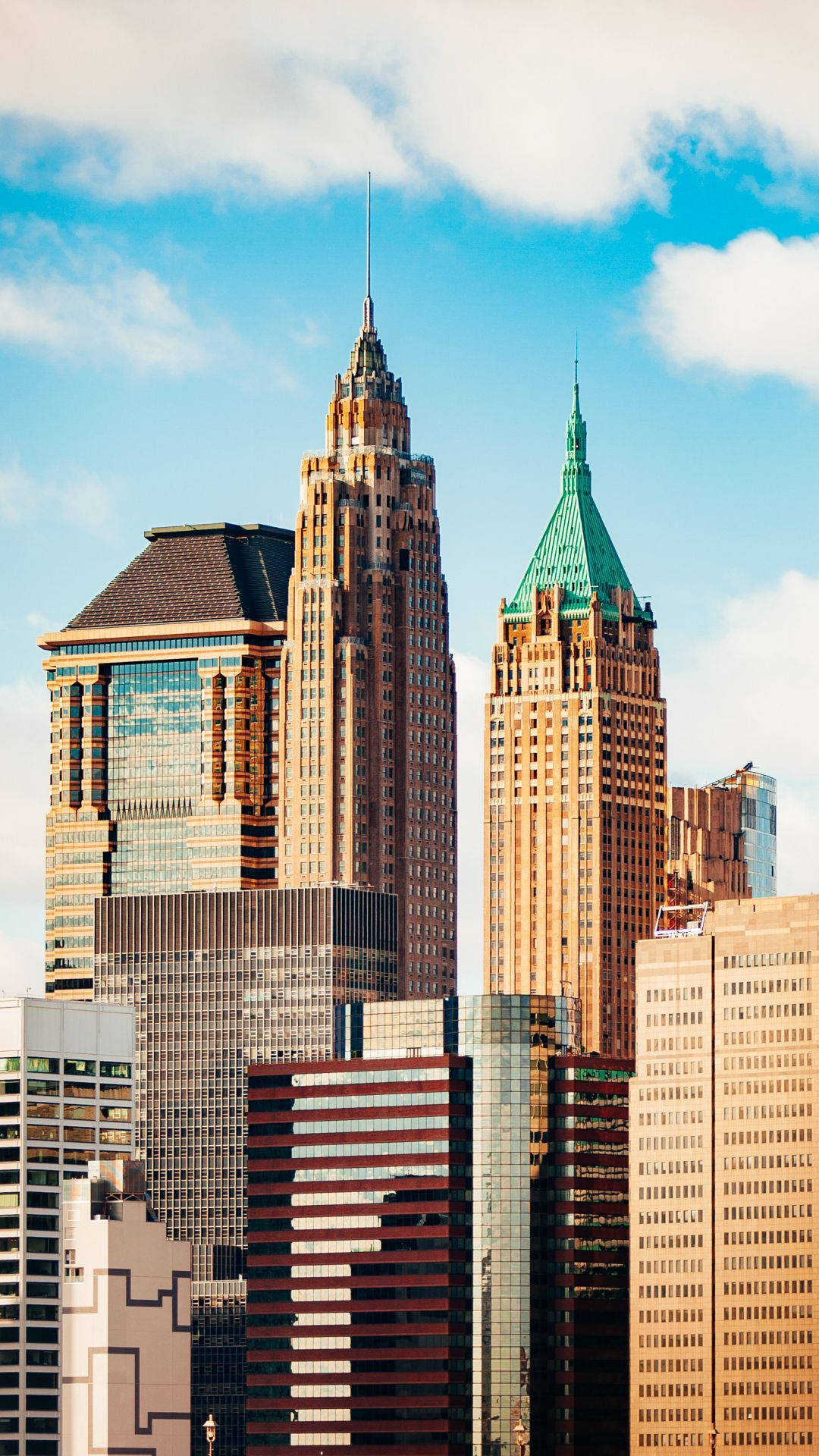 New York 桌布 壁紙 — 高聳入雲的摩天大樓，玻璃和石材外牆刺破點綴著蓬鬆白雲的明亮藍天。