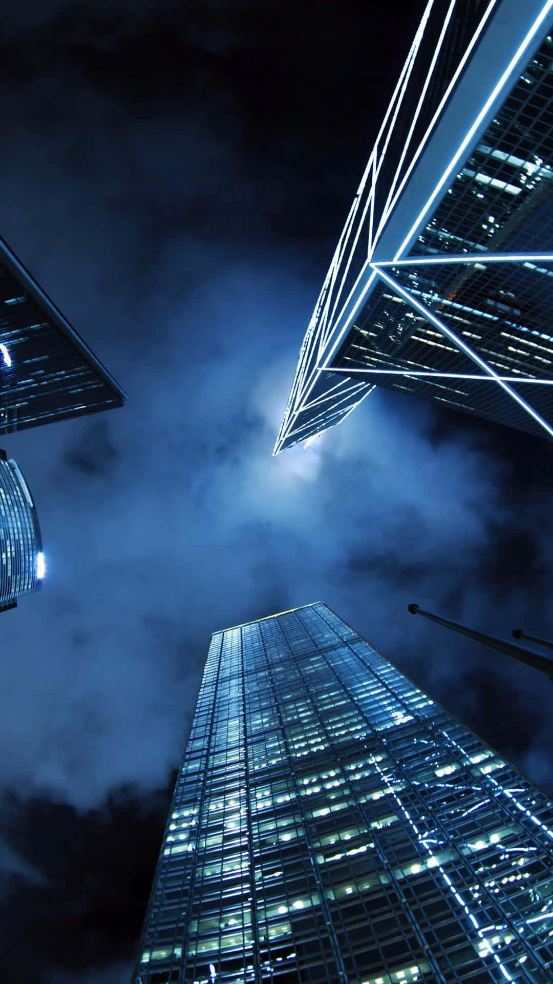 Modern Aesthetic 桌布 壁紙 — 高聳入雲的摩天大樓刺穿陰沉的夜空，玻璃外牆在旋轉的雲層中閃爍著電光藍色的光芒。