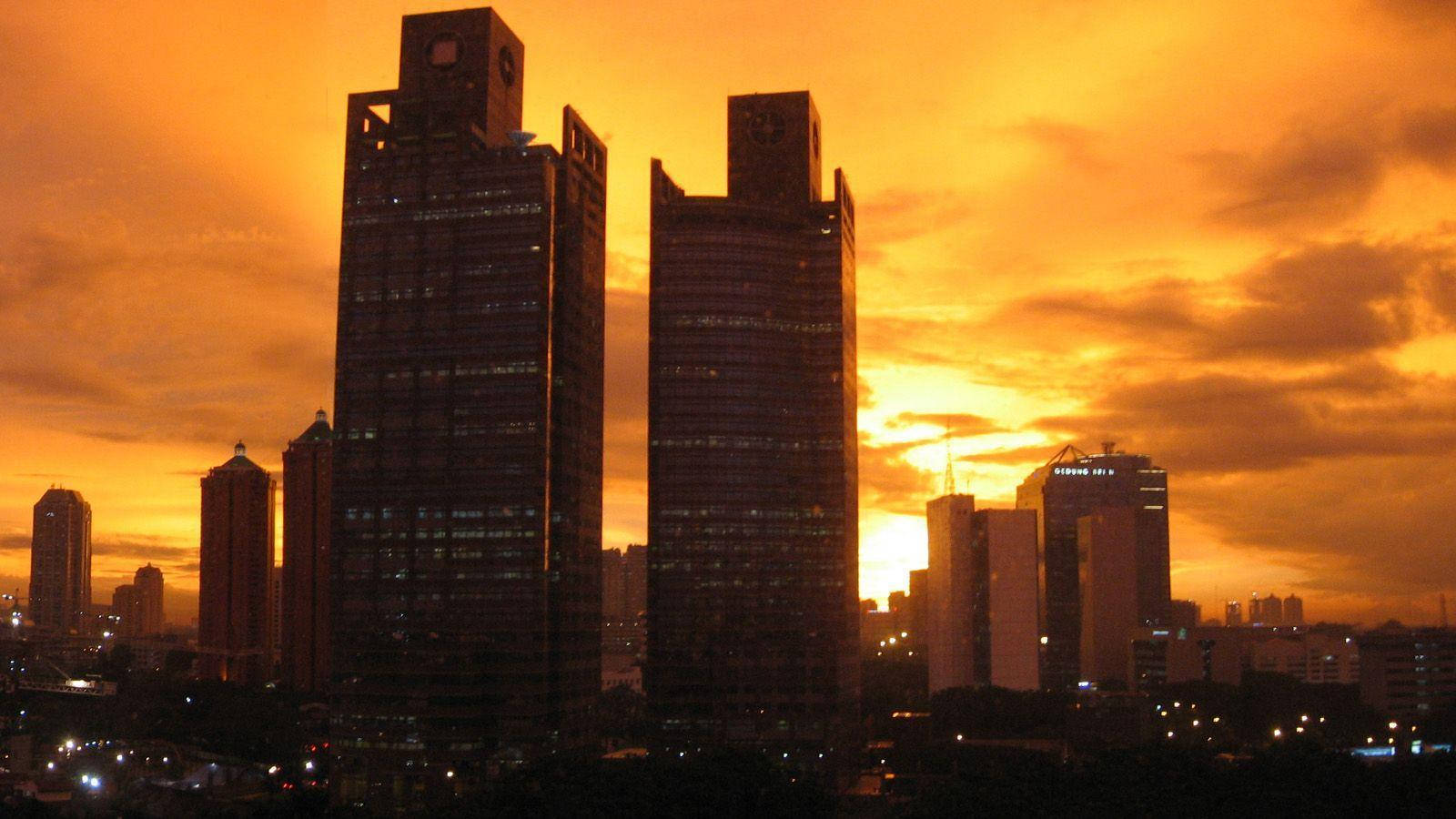Jakarta 桌布 壁紙 — 高聳入雲的摩天大樓在火紅橙色的日落天空襯托下形成剪影，天空中有零星雲朵。