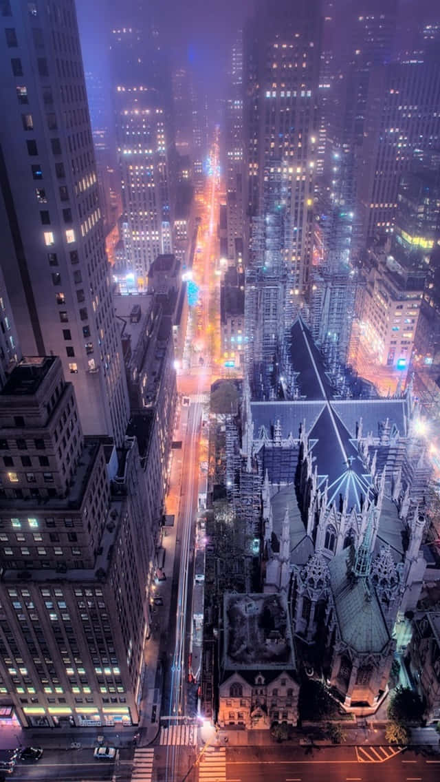 New York City Night iPhone 桌布 壁紙 — 高聳摩天大樓中，一條繁華城市街道夜晚的鳥瞰圖，燈火輝煌，還有一座哥德式教堂。