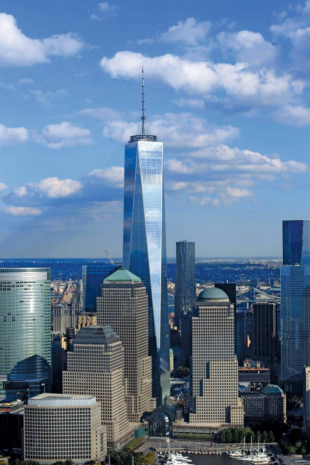 Blue Sky 桌布 壁紙 — 高聳的One World Trade Center在明亮的藍天下閃耀，天空點綴著蓬鬆的白雲，下方是密集的城市天際線。