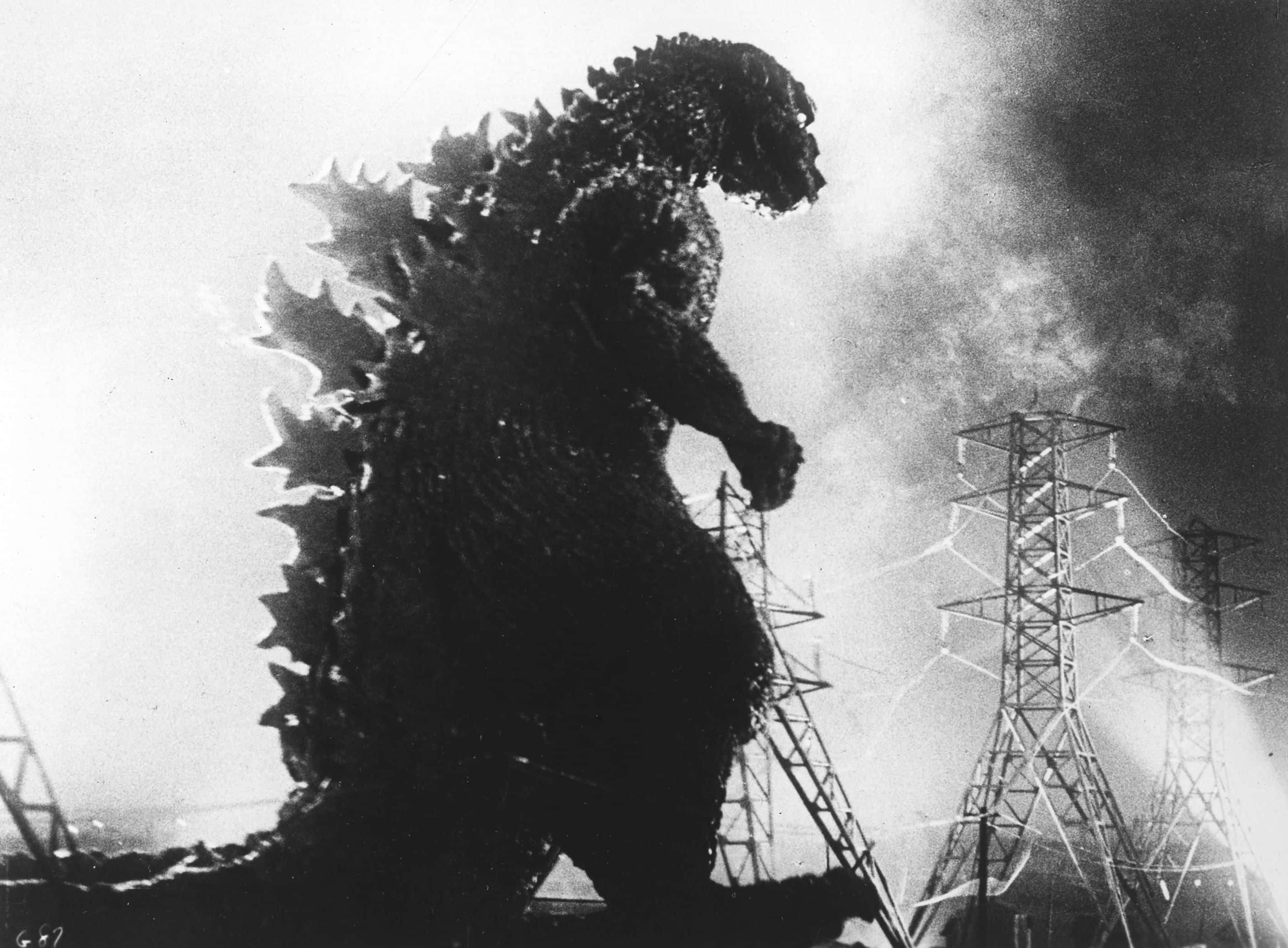 Godzilla 1954 桌布 壁紙 — 高聳的哥吉拉剪影穿過煙霧，旁邊是受損的電塔，構成戲劇性的黑白場景。