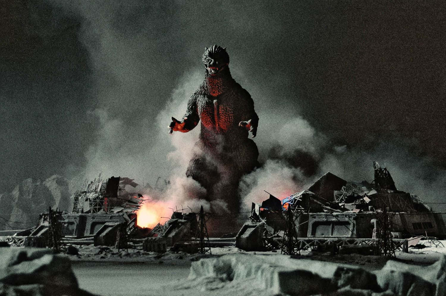 Classic Godzilla 桌布 壁紙 — 高聳的哥吉拉站在白雪覆蓋的廢墟中，熾熱的爆炸照亮了黑暗的夜空。