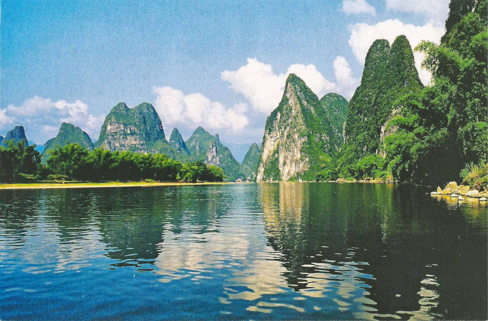 Ivory 桌布 壁紙 — 高聳的喀斯特山脈覆蓋著茂密的綠色植物，在晴朗的天空和蓬鬆的雲朵下從平靜的藍色海水中升起。